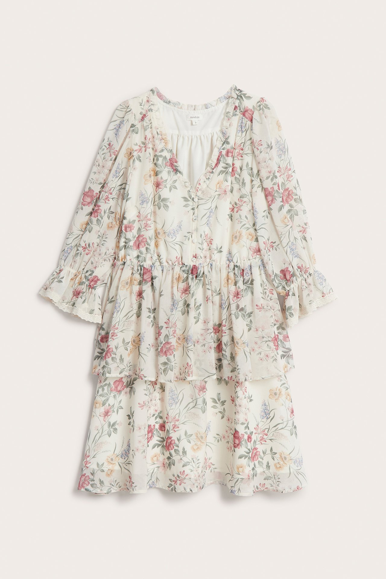 Forfra, offwhite blomstret chiffonkjole med volanger, tildekkede knapper og halvlange elastiske ermer.