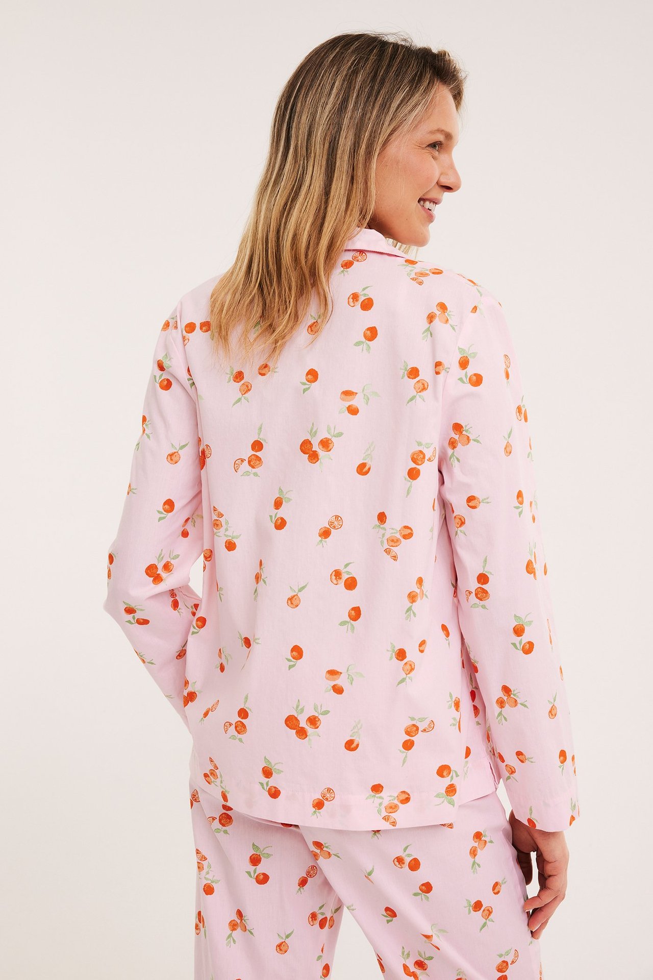 Selkäkuva: Nainen vaaleanpunaisessa oranssikuvioisessa puuvillapyjamapaidassa ja samanlaiset housut.