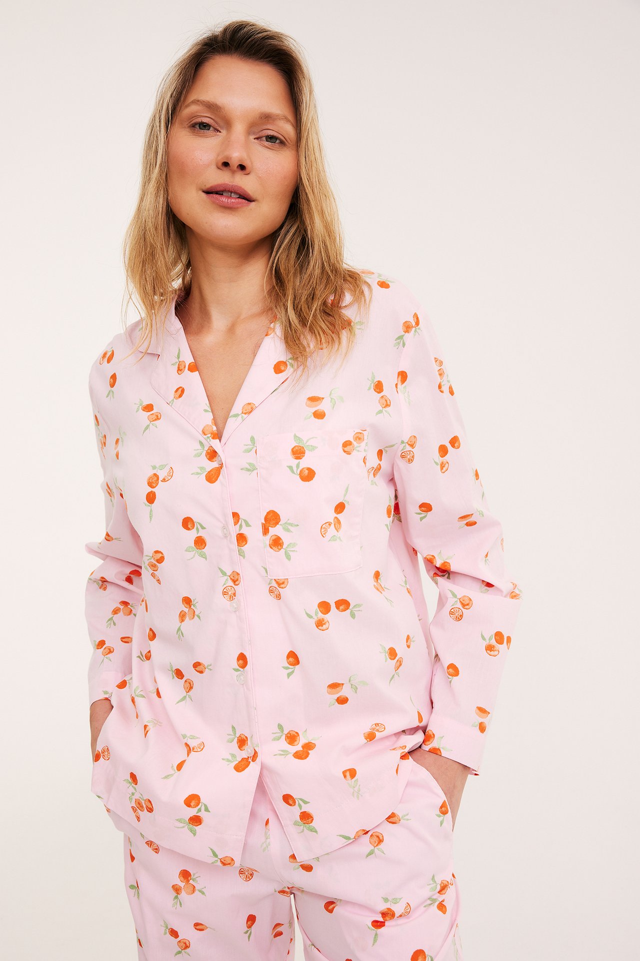 Edestä: Nainen vaaleanpunaisessa kudotussa puuvillapyjamapaidassa hedelmäkuviolla ja yhteensopivissa housuissa.