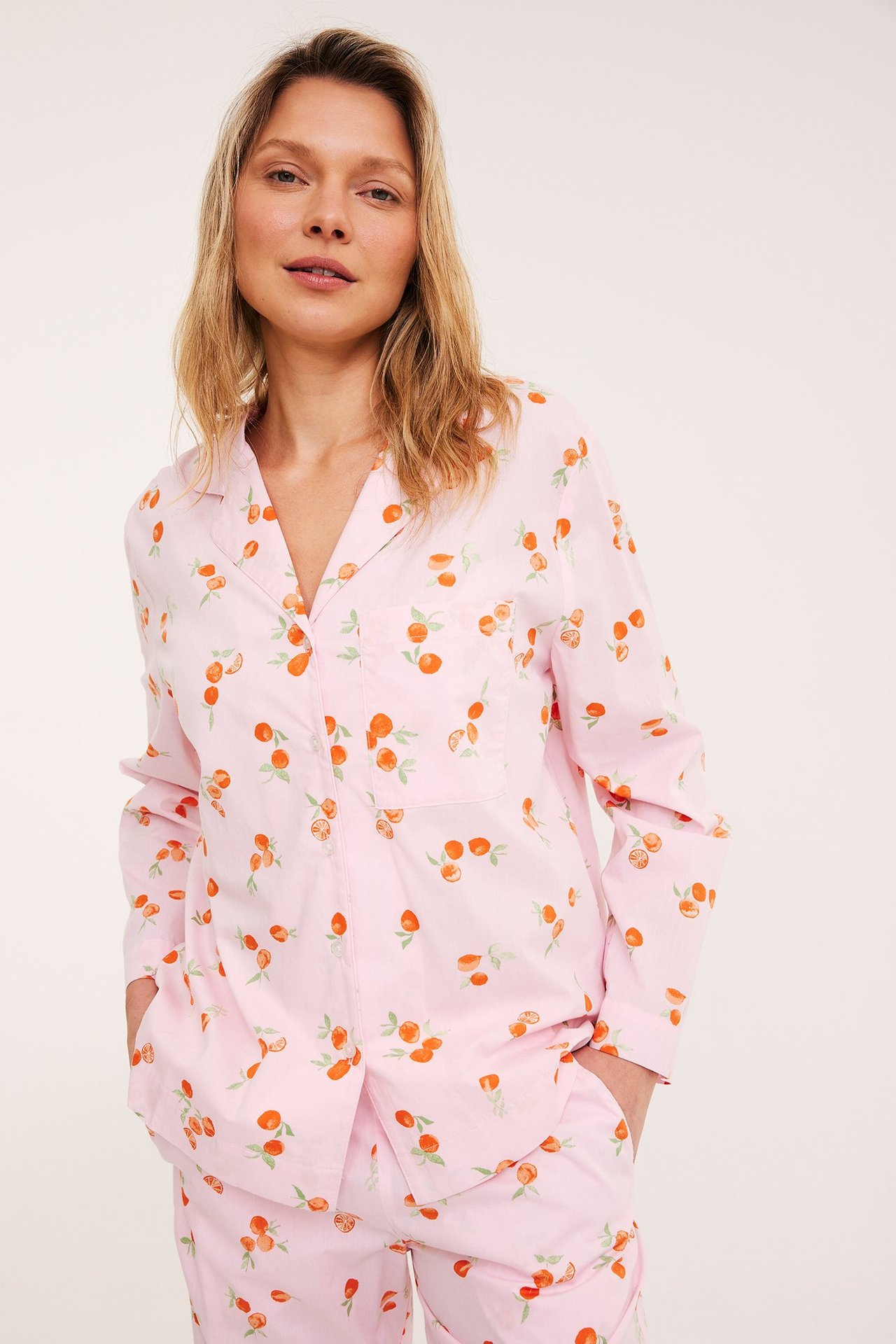 Edestä: Nainen vaaleanpunaisessa kudotussa puuvillapyjamapaidassa hedelmäkuviolla ja yhteensopivissa housuissa.