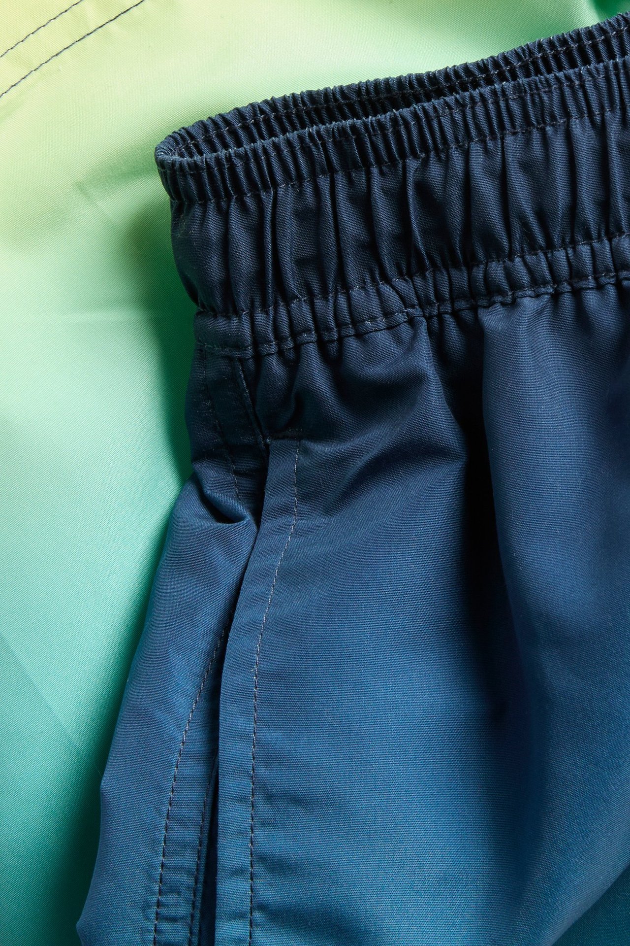 Zbliżenie na niebieskie szorty kąpielowe z efektem ombre, z elastyczną talią i boczną kieszenią.