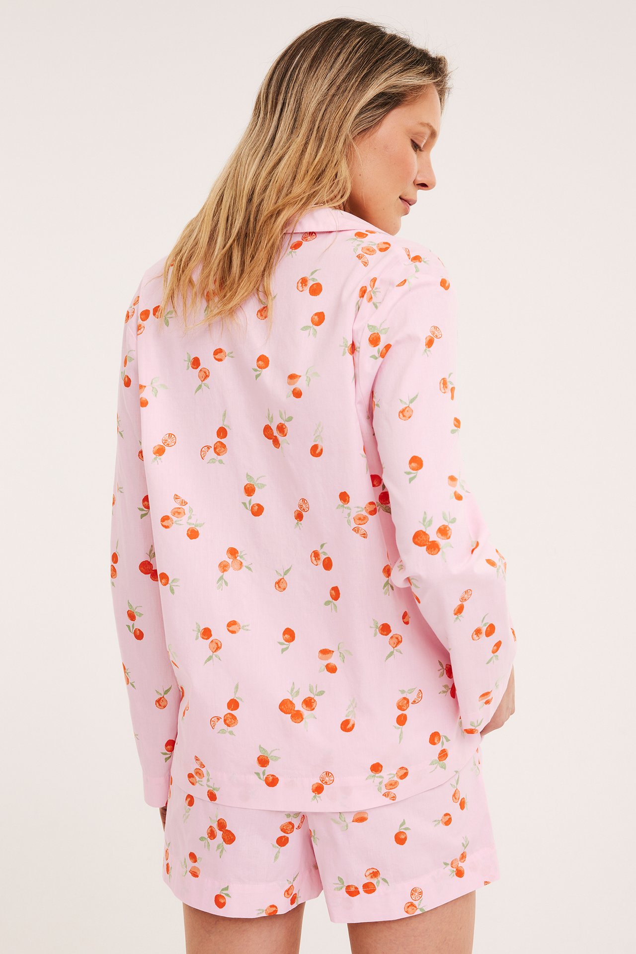 Naisen selkäpuolelta: Vaaleanpunaiset puuvillapyjamashortsit appelsiinikuviolla ja yhteensopiva toppi.