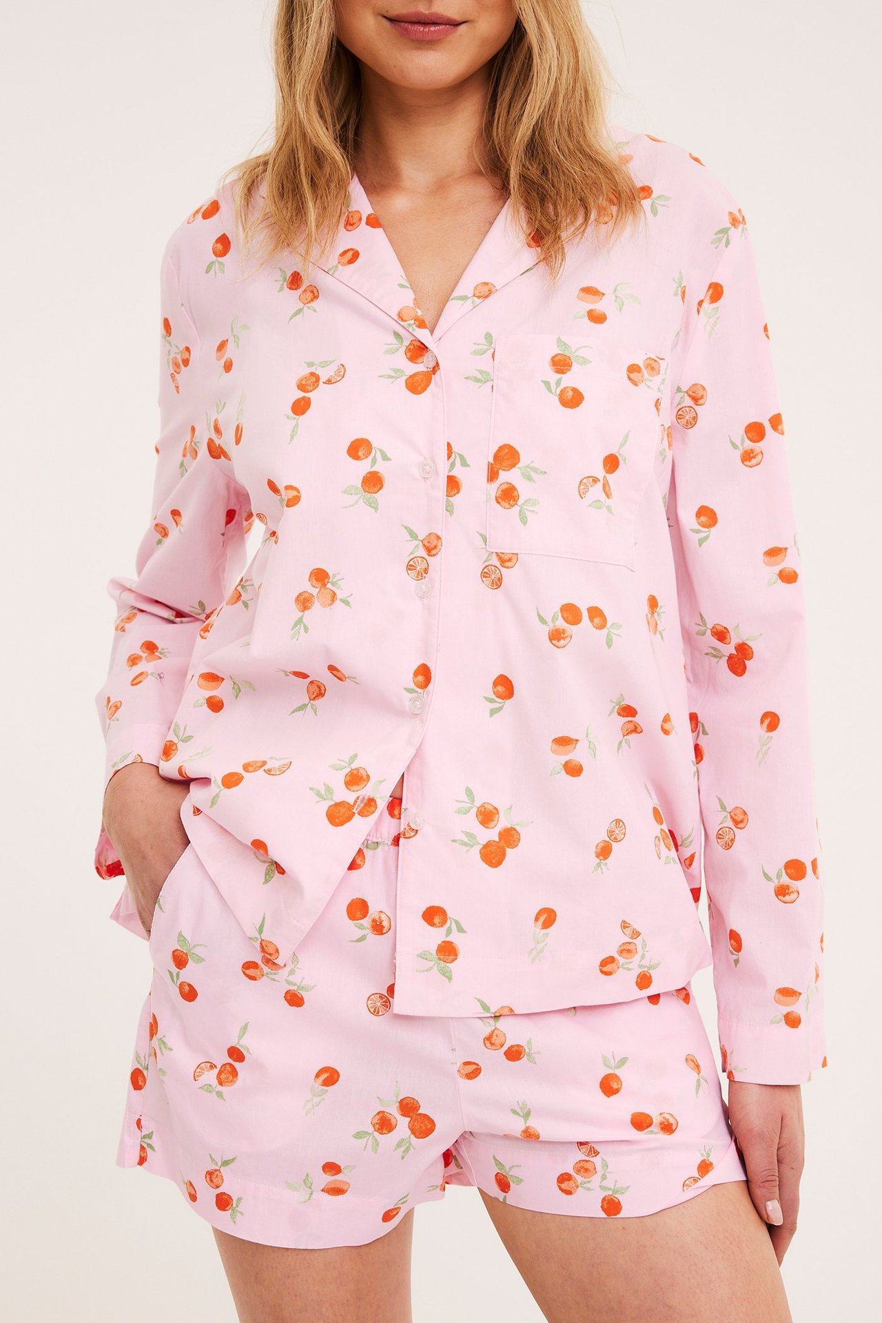 Edestä näkymä: Nainen yllään vaaleanpunaiset puuvillapyjamashortsit hedelmäkuviolla ja yhteensopiva pitkähihainen paita.