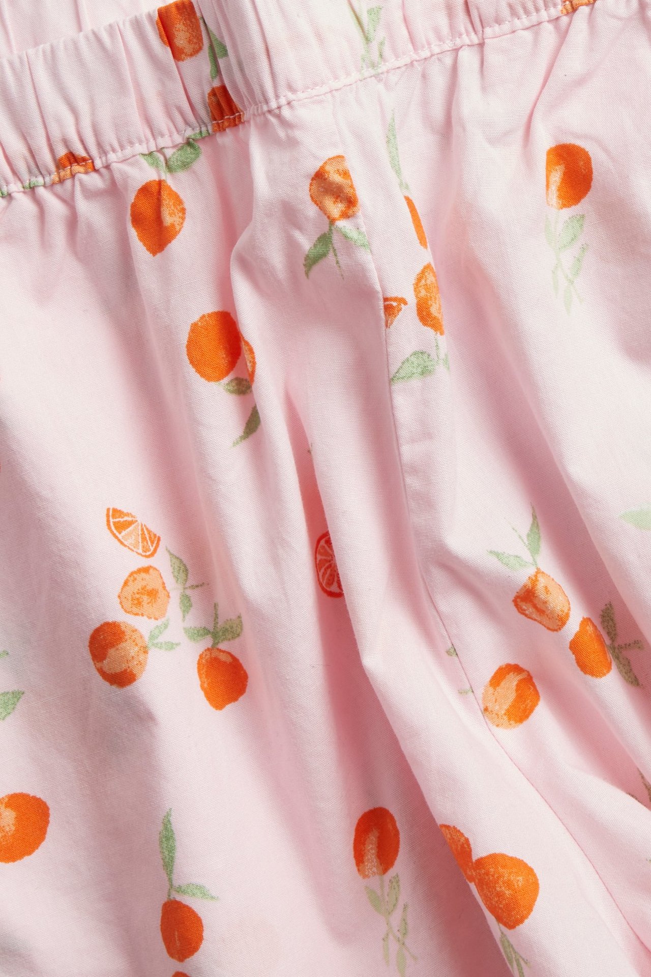 Zbliżenie na jasnoróżowe, bawełniane szorty piżamowe z elastyczną talią i wzorem w owoce.