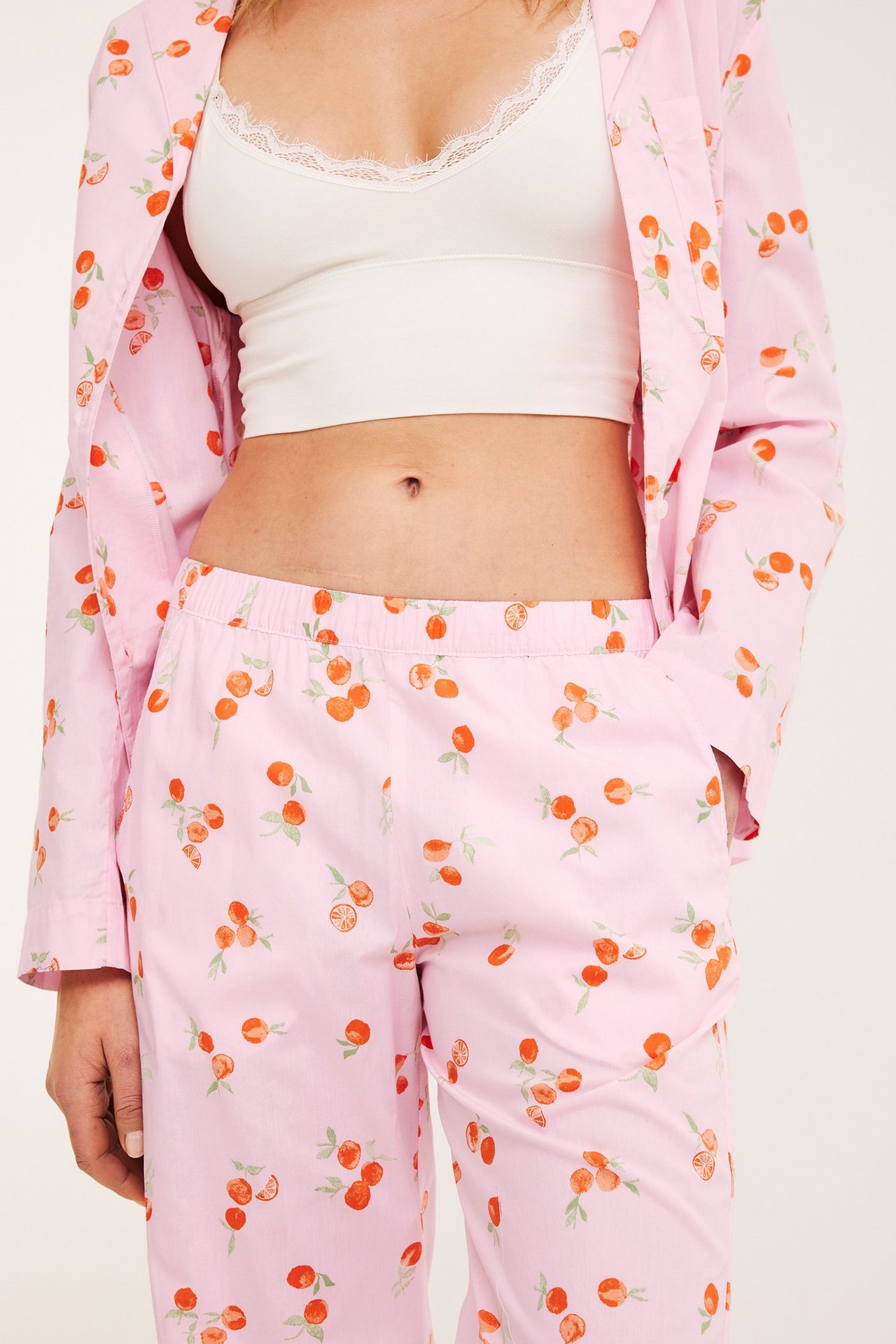 Etunäkymä: Nainen vaaleanpunaisissa pyjamahousuissa hedelmäkuviolla, yhteensopiva avoin takki, valkoinen rintaliivit.