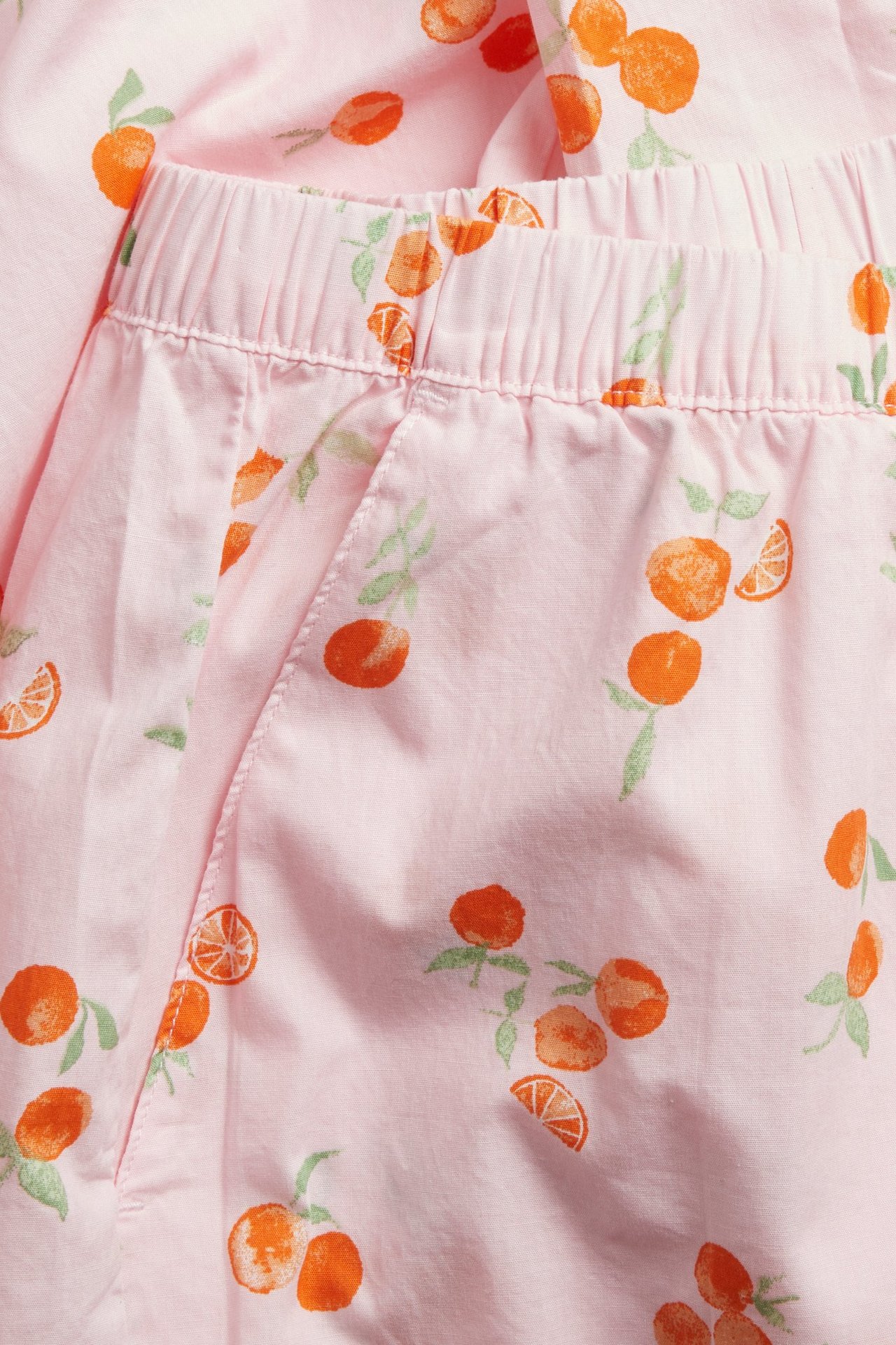 Zbliżenie jasnoróżowych bawełnianych spodni piżamowych w pomarańczowy wzór, z gumką w pasie i kieszenią.