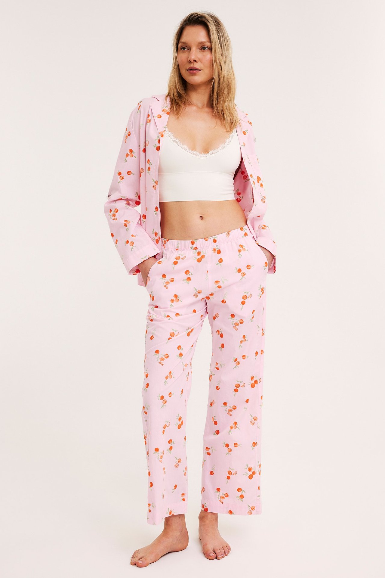 Nainen vaaleanpunaisissa kirsikkaprintti puuvillapyjamahousuissa, avoimessa paidassa ja valkoisessa pitsitopissa, edestäpäin.