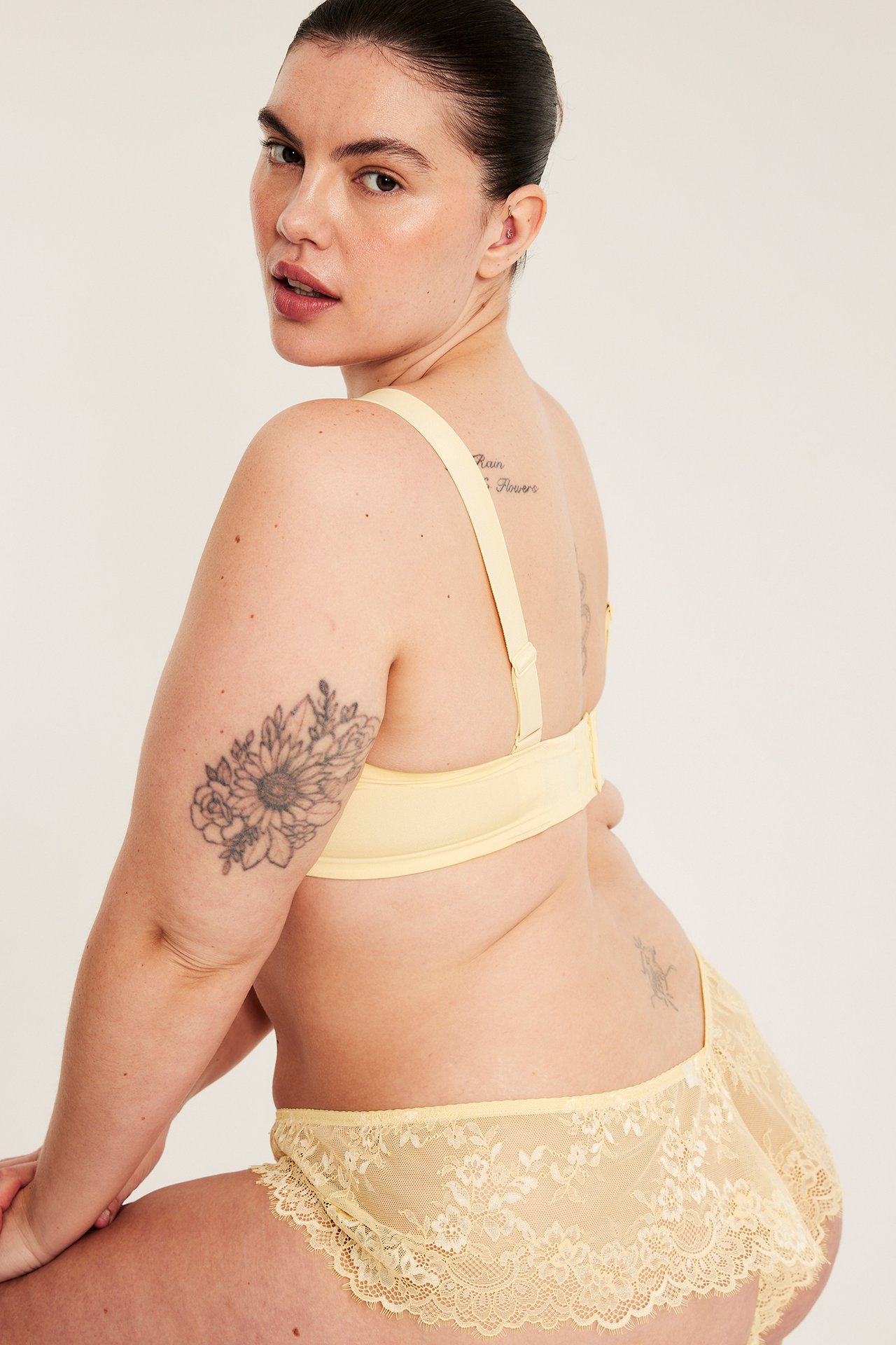 Sidovy av en kvinna i ljusgula, höga spetstrosor med franskanter och matchande behå.