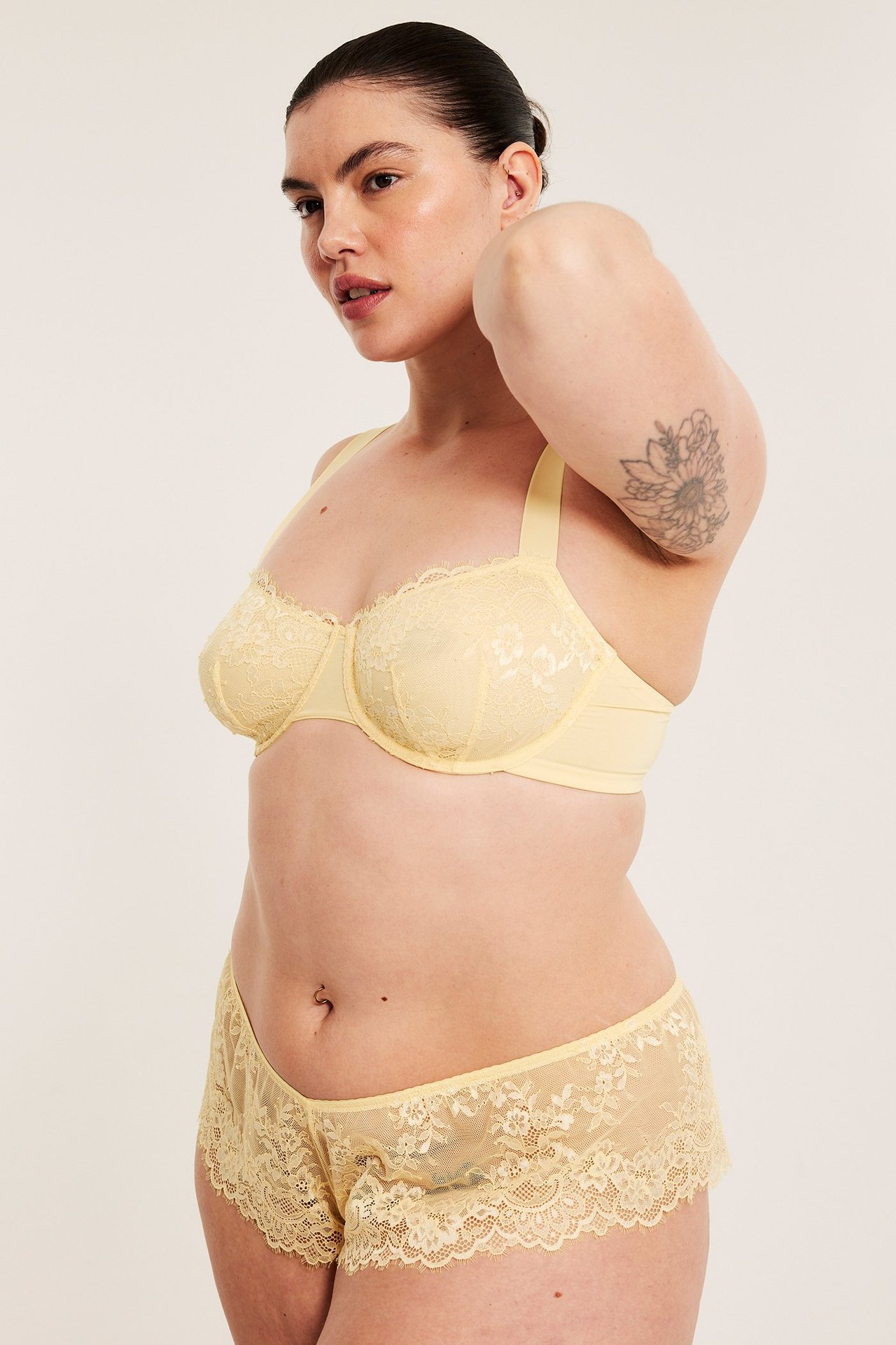 Sivukuva naisesta, yllään vaaleankeltaiset pitsipikkuhousut ja yhteensopivat pitsirintaliivit.