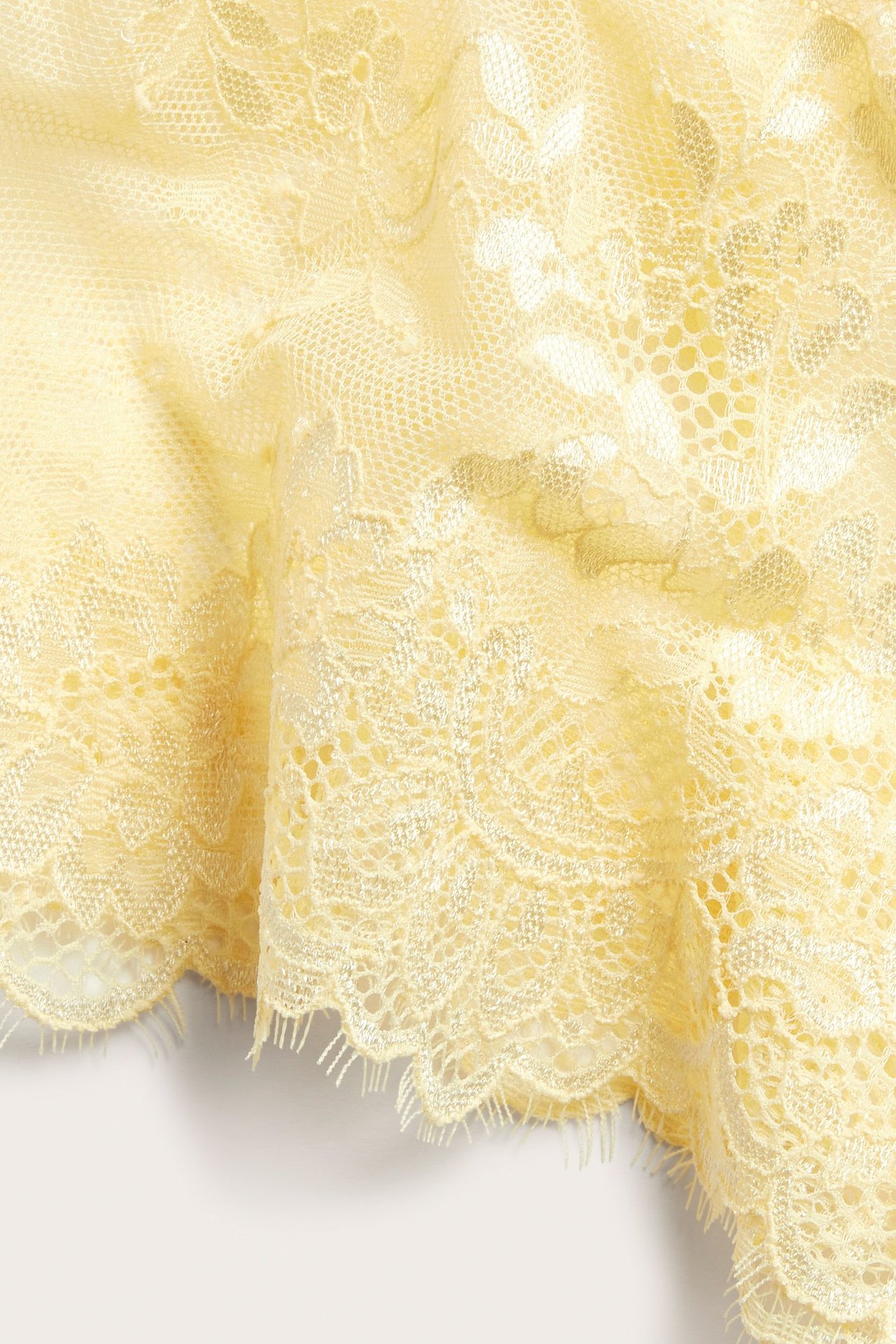 Zbliżenie jasnożółtego koronkowego materiału fig z falistym brzegiem i kwiatowym wzorem.