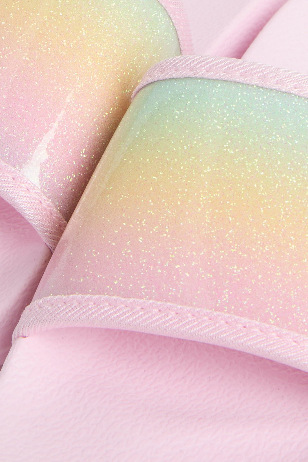 Närbild av två rosa sandaler med en glittrig ovandel i gradient av rosa, gult och ljusgrönt.