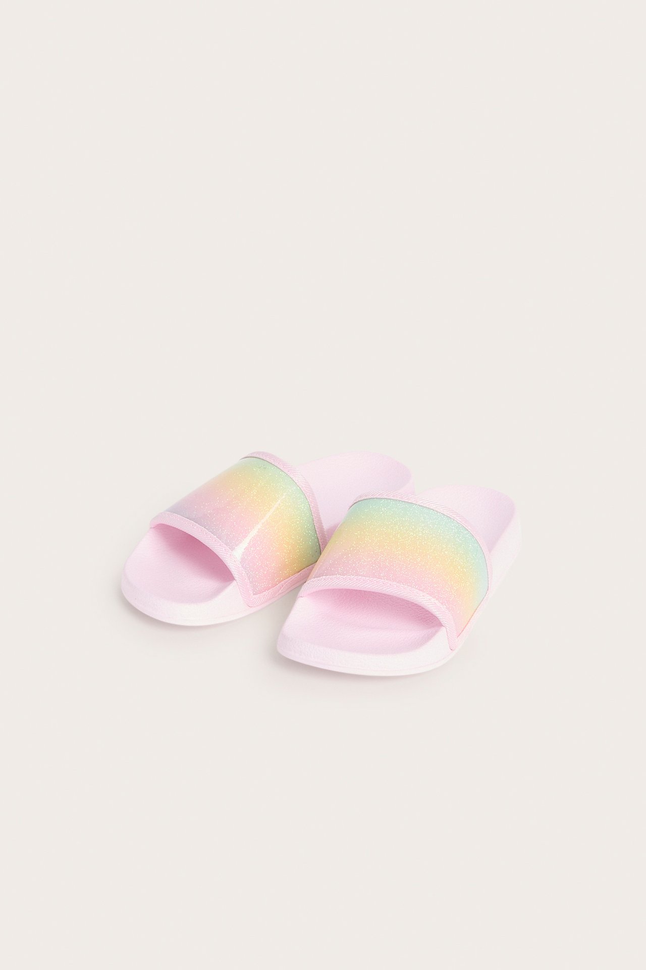 Toppvy av två rosa plasttofflor för barn med glittriga regnbågsfärgade remmar.