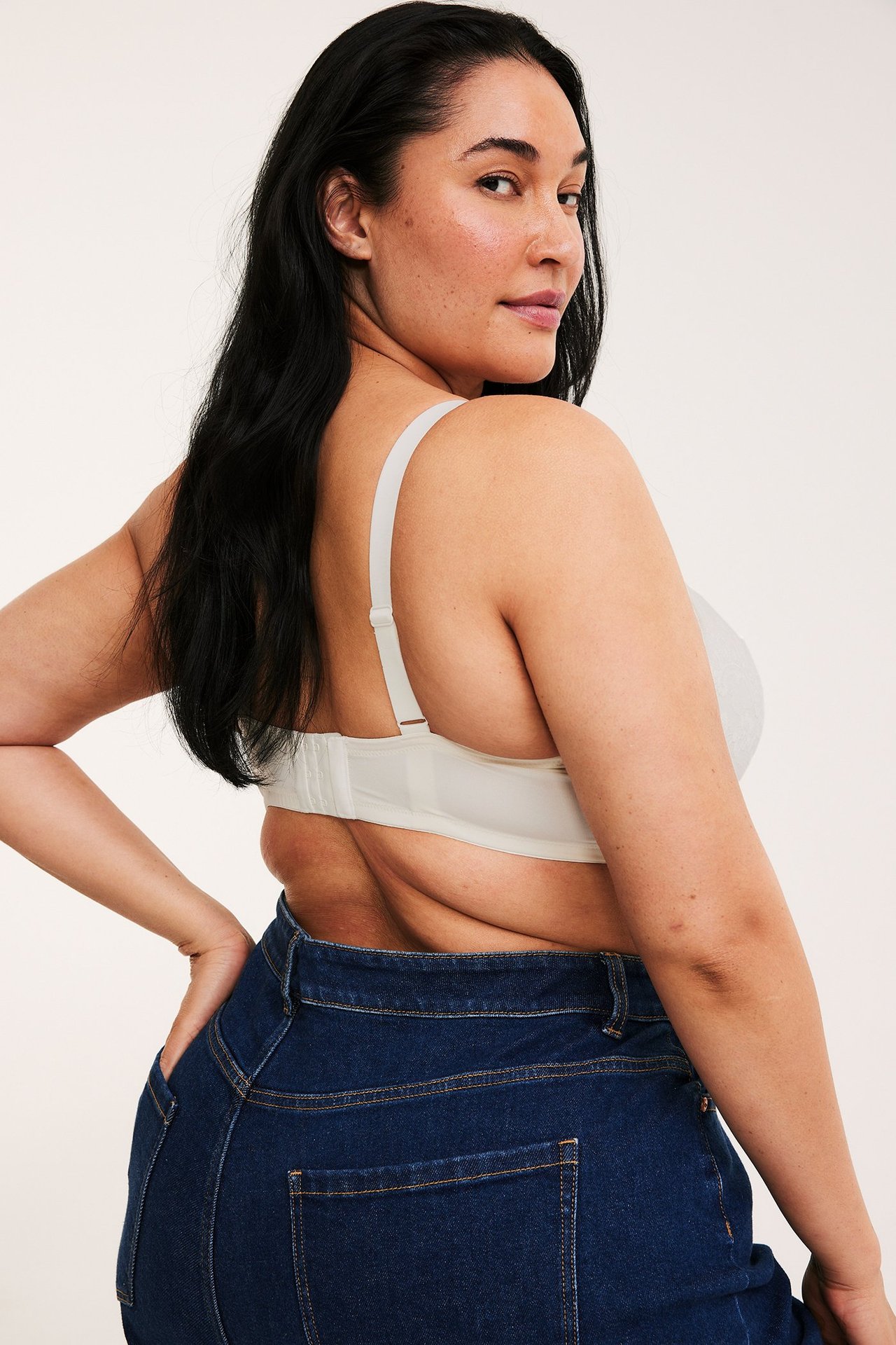 Kvinna bakifrån/sida i offwhite spets push-up behå med justerbara band och mörkblå jeans.