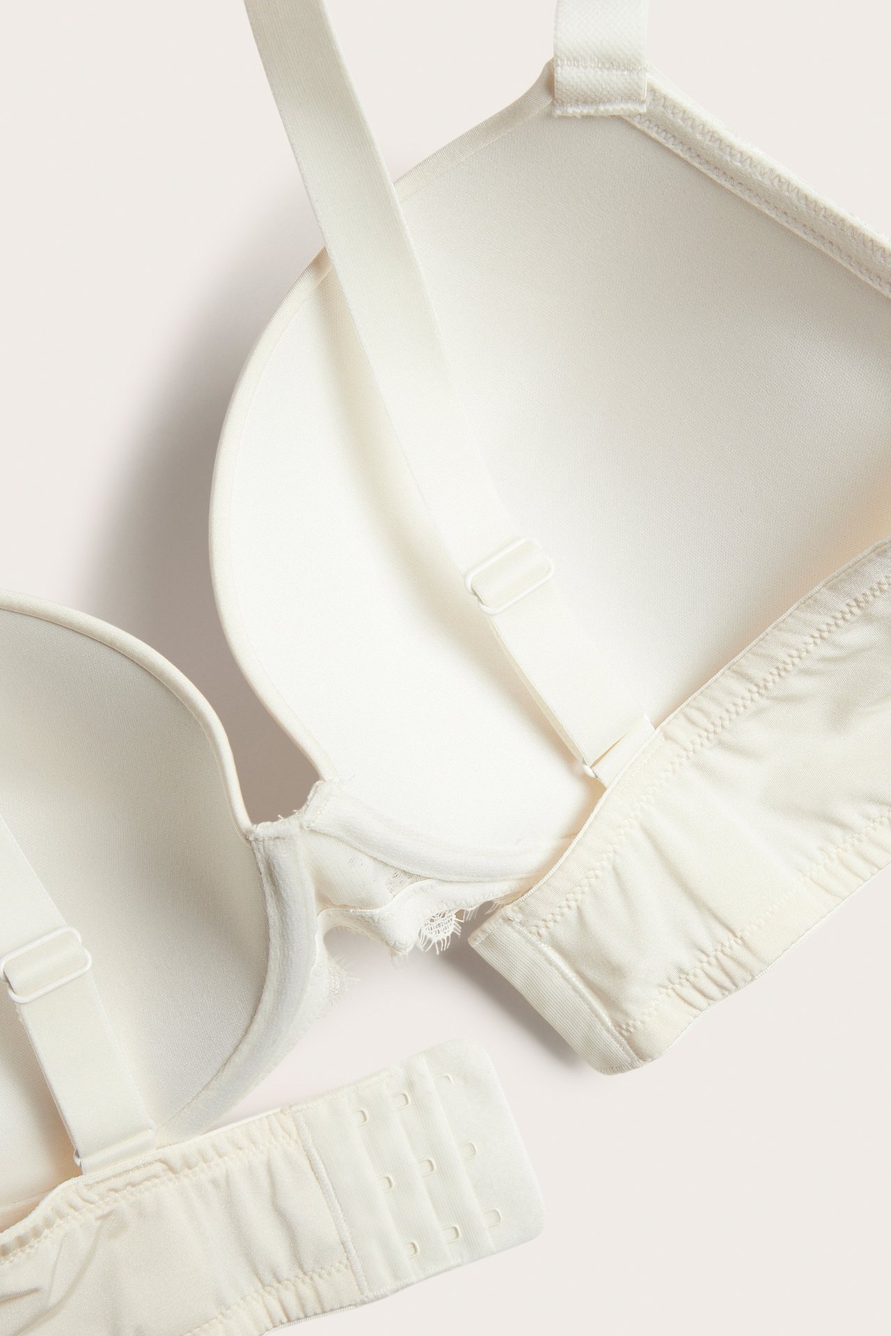 Närbild på en offwhite push-up bh med spetsklädda kupor, justerbara axelband och hyskknäppning.