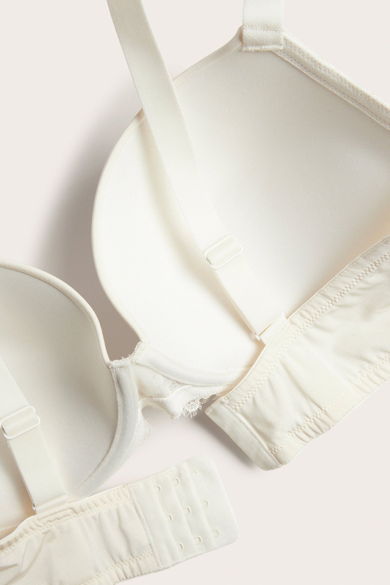 Närbild på en offwhite push-up bh med spetsklädda kupor, justerbara axelband och hyskknäppning.