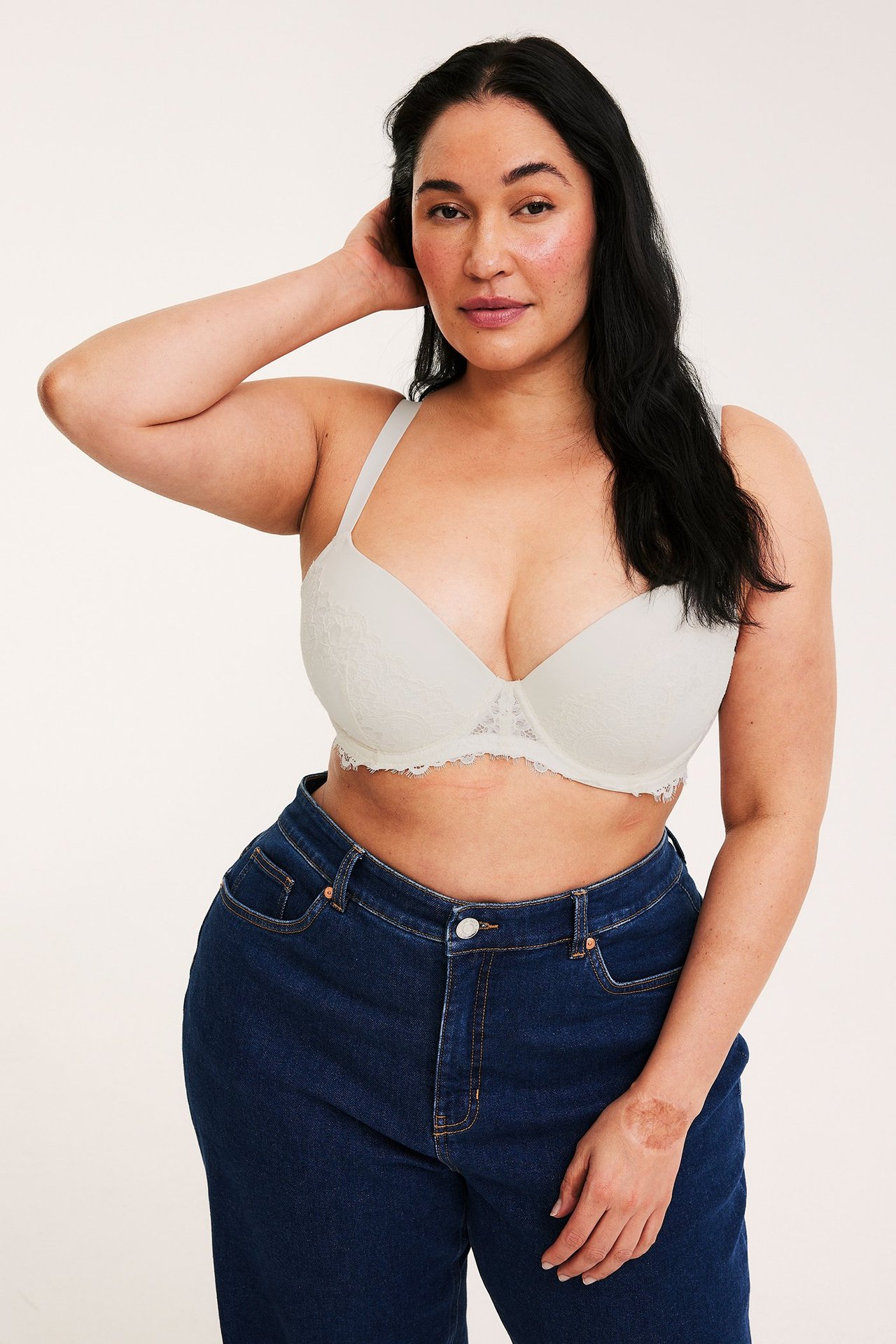 Frontvy av en kvinna som bär en offwhite spets push-up behå och mörkblå jeans.