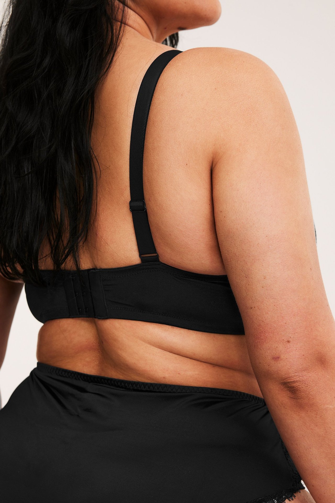 Ryggvy av en kvinna i svart push-up BH med justerbara band, hakstängning och svarta trosor.