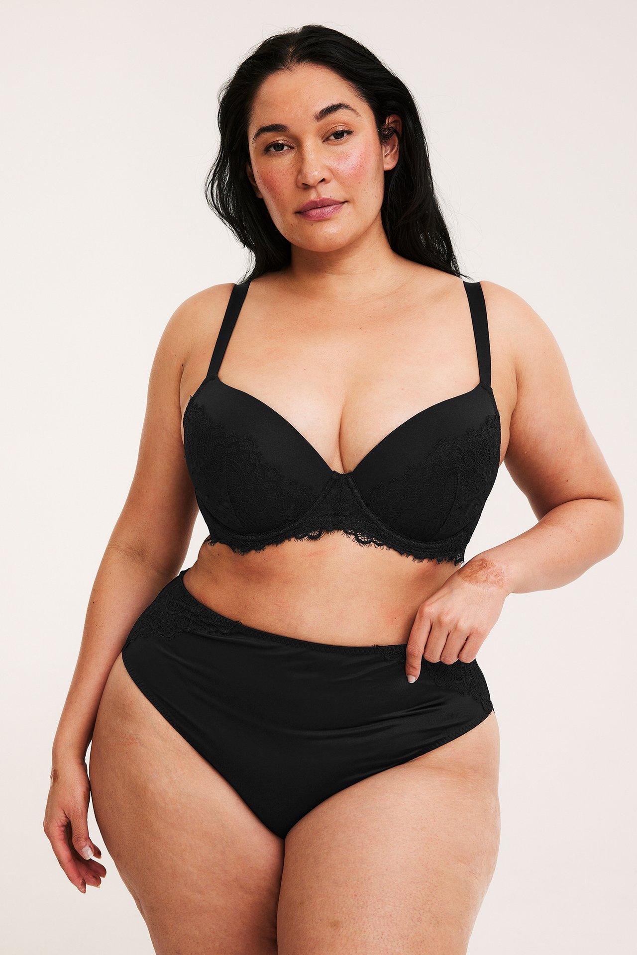 Naisen etukuva, yllään mustat pitsi push-up rintaliivit ja mustat korkeavyötäröiset pitsialushousut.