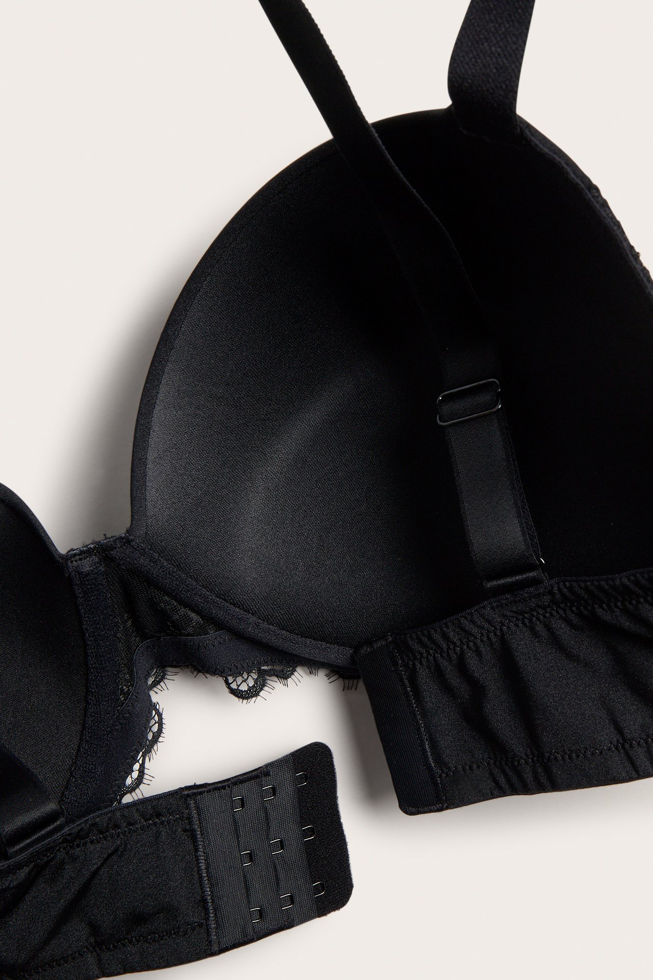 Närbild av en svart push-up BH med spetsklädda kupor, mikrofiber och synlig hysk- och hakknäppning.