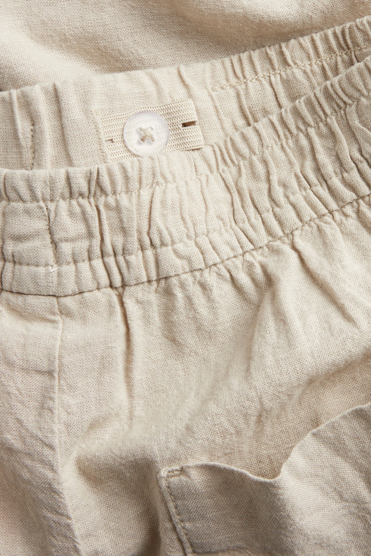 Lähikuva beigestä pellavasekoiteshortseista, joissa joustava vyötärö ja säädettävä nappi sisäresorissa.