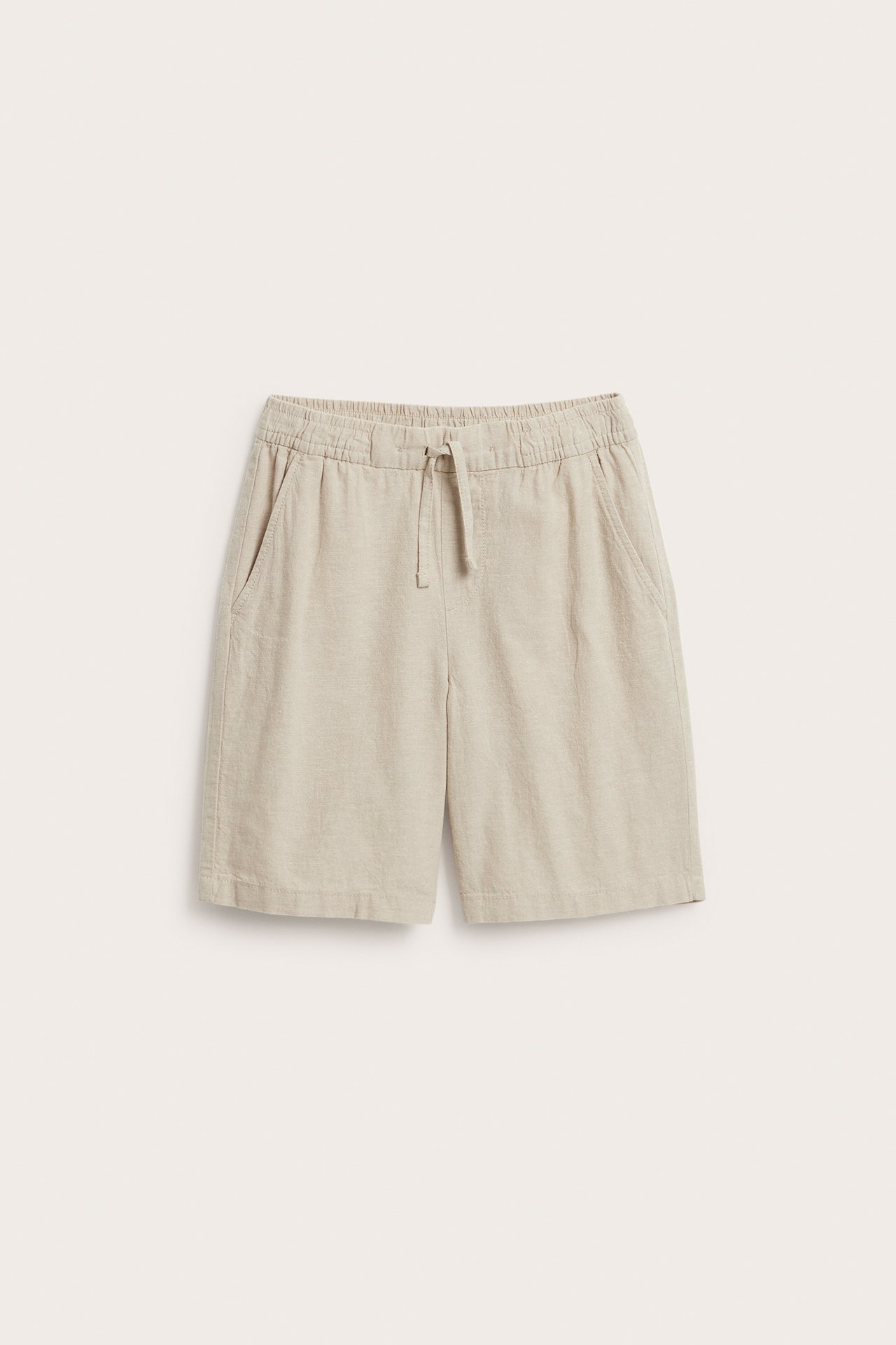 Edestäpäin: lasten beiget pellavasekoiteshortsit joustavalla kiristysnyörivyötäröllä ja sivutaskuilla.