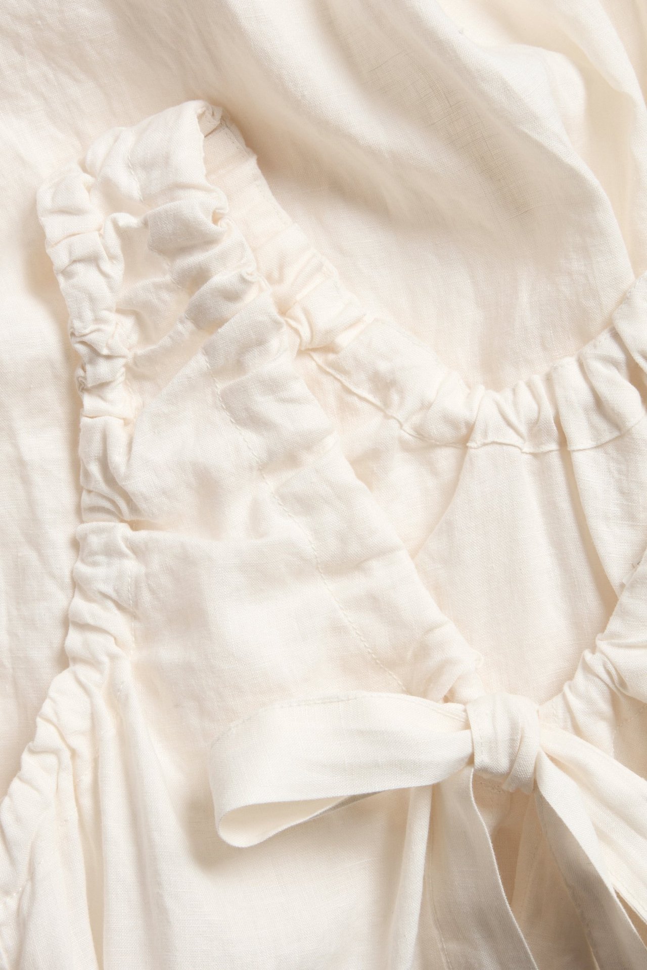 Zbliżenie białej, lnianej sukienki bez rękawów, z marszczonym dekoltem w serek i wiązaniem.