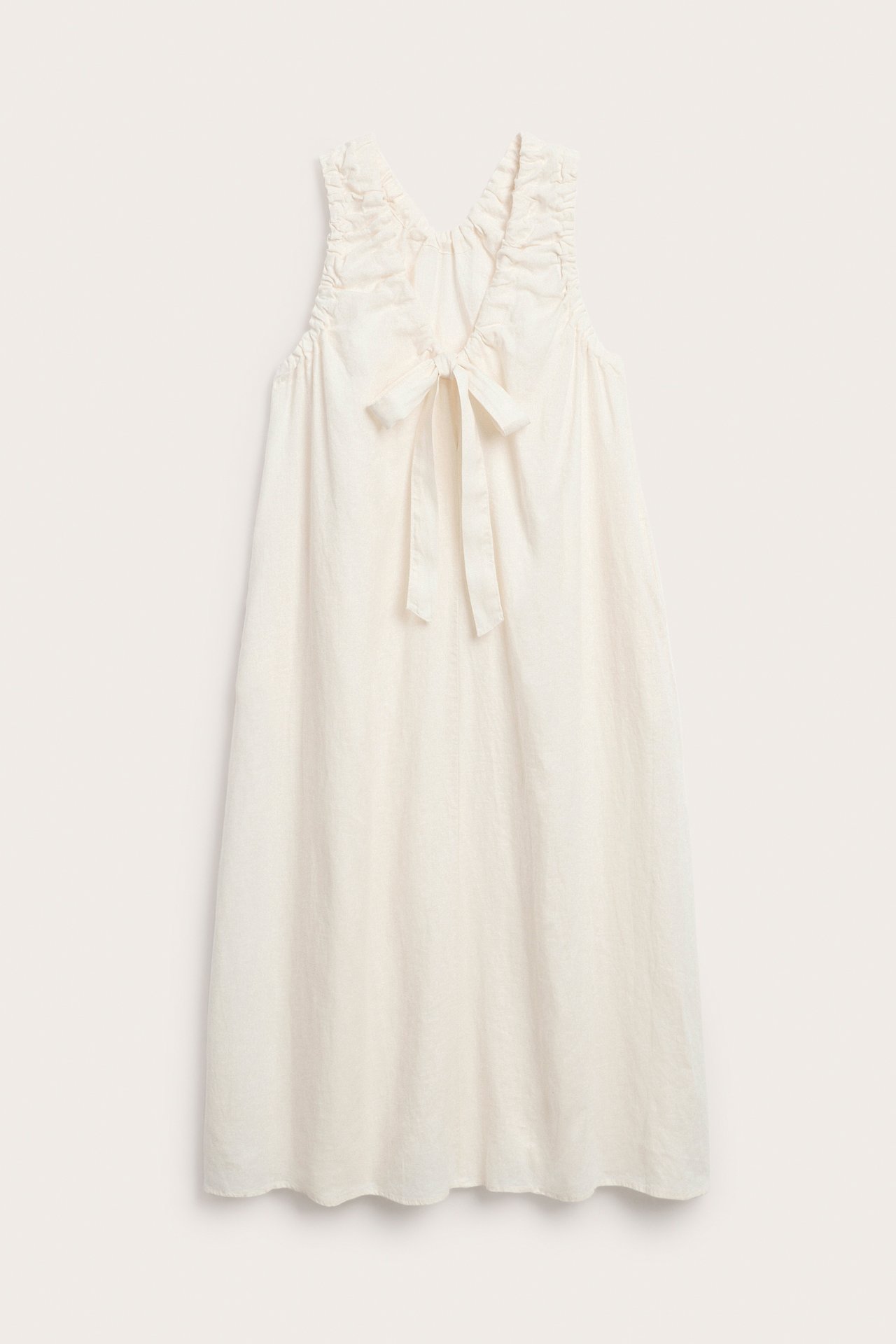 Biała, lniana sukienka bez rękawów, z marszczonymi pachami i wiązaniem na plecach.