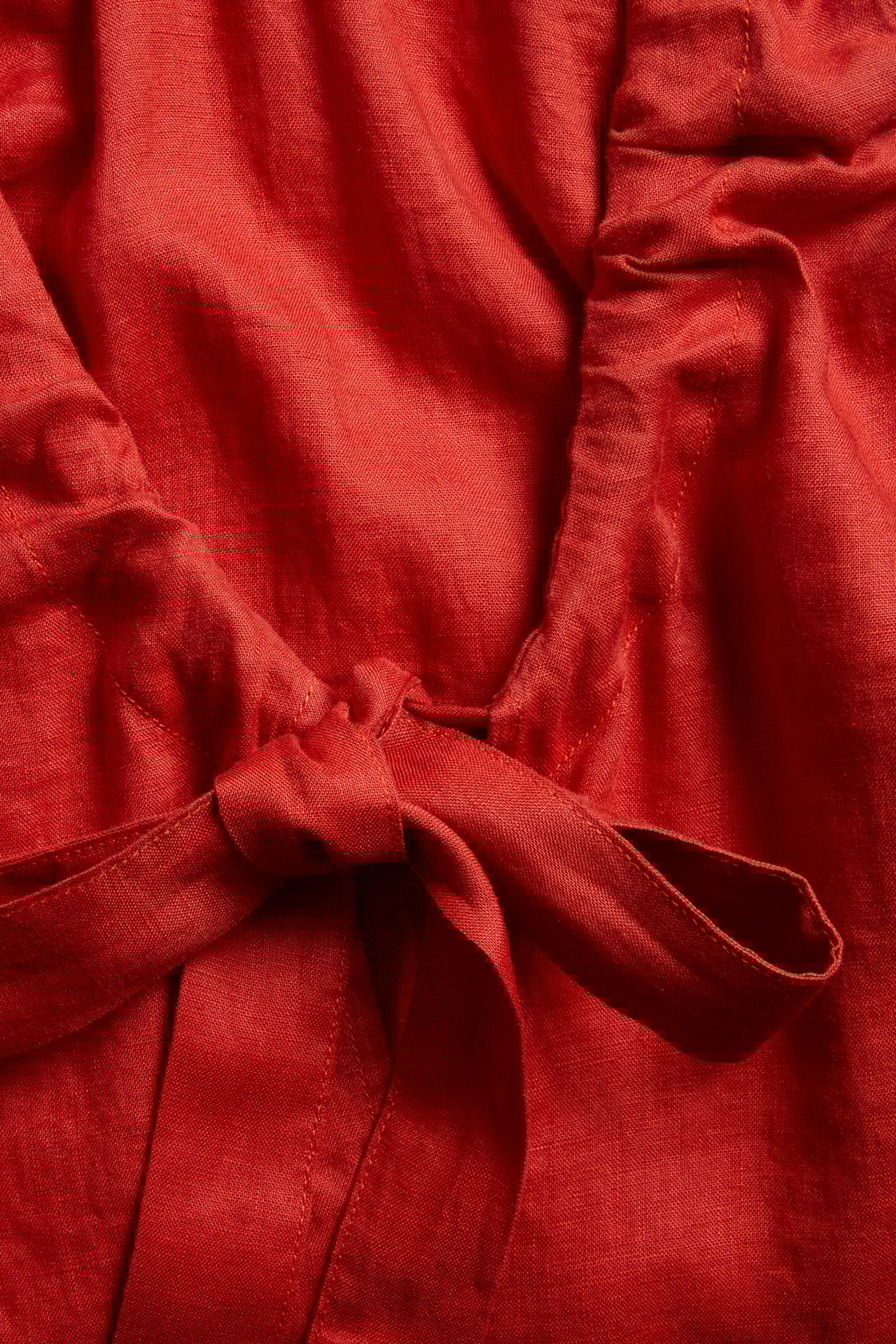 Zbliżenie czerwonej lnianej sukienki, ukazujące wyraźne wiązanie przy dekolcie w serek.