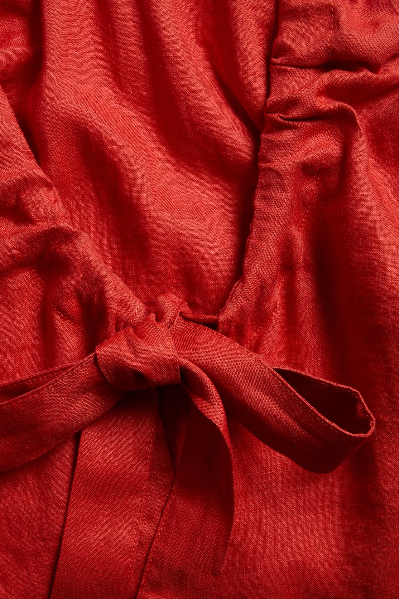 Zbliżenie czerwonej lnianej sukienki, ukazujące wyraźne wiązanie przy dekolcie w serek.