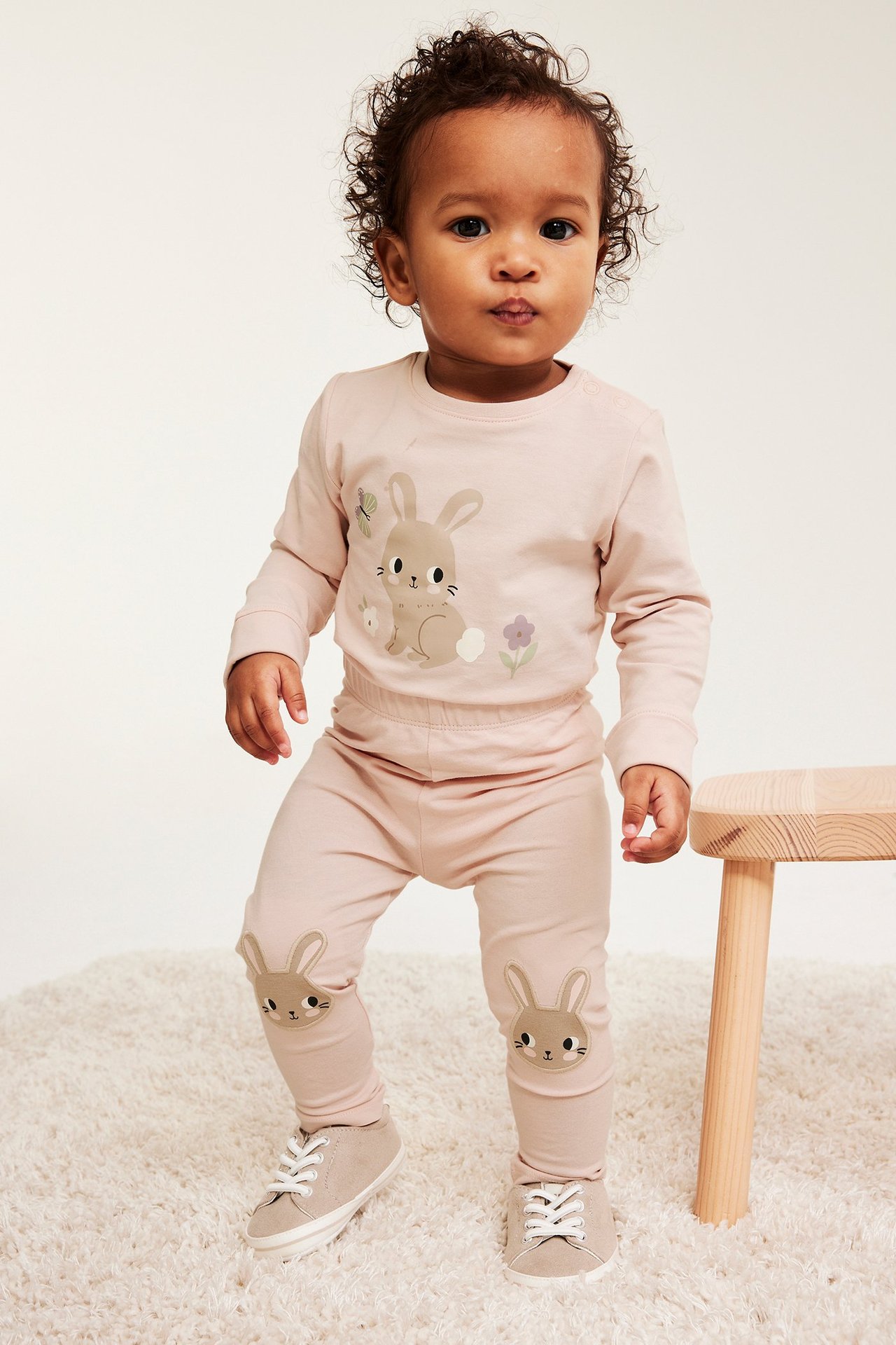 Etunäkymä: Vauva yllään vaaleanpunainen pupupainettu body, yhteensopivat legginsit pupupolvitilkkuineen ja beiget kengät.