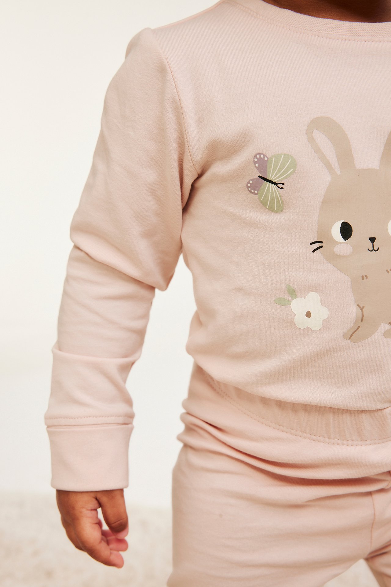 Lähikuva vauvasta, yllään vaaleanpunainen pitkähihainen puuvillabody pupu- ja perhoskuviolla ja taitettavilla hihansuilla.