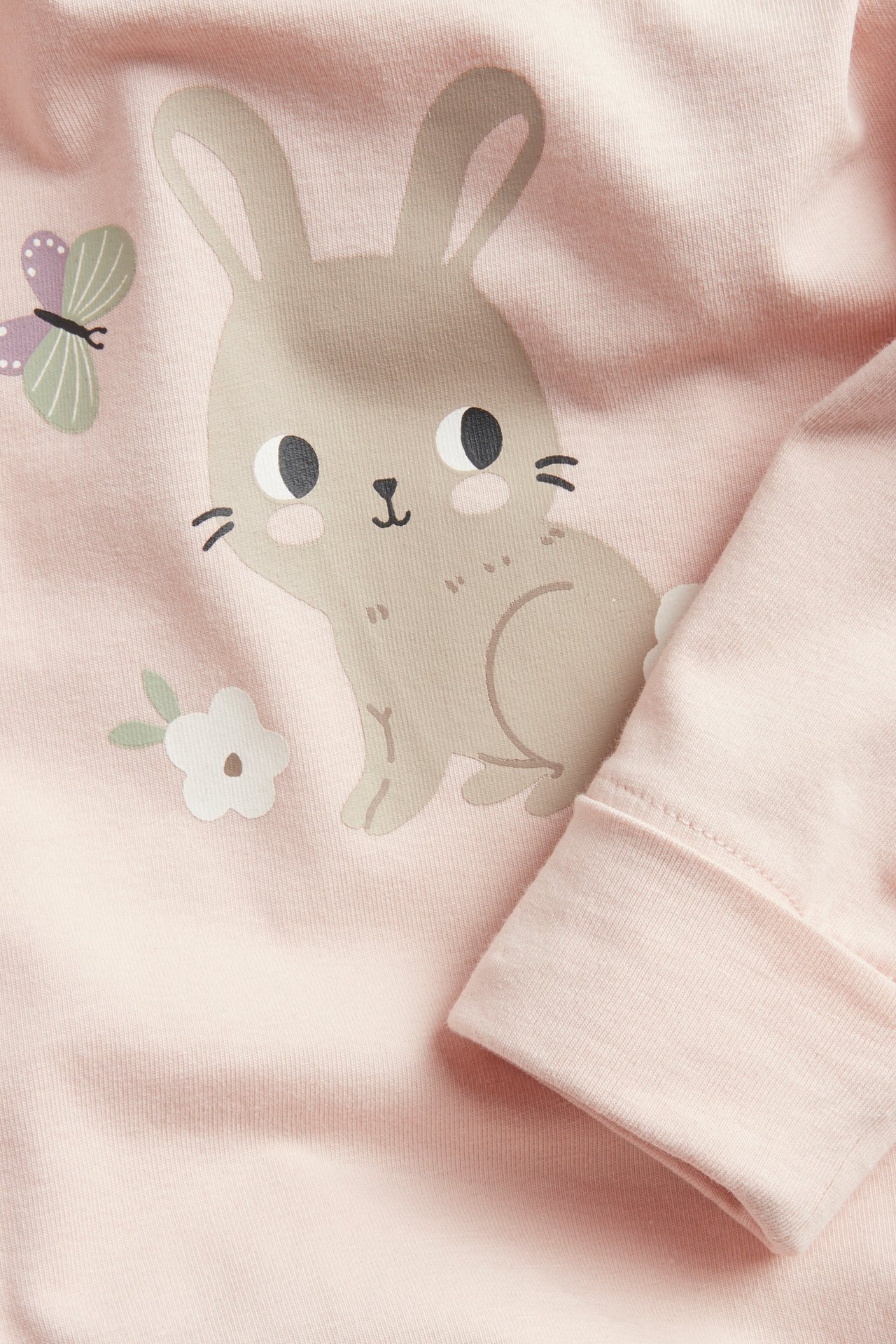 Lähikuva vauvan vaaleanpunaisesta puuvillabodysta, jossa on pupu- ja perhoskuvio, hiha näkyvissä.