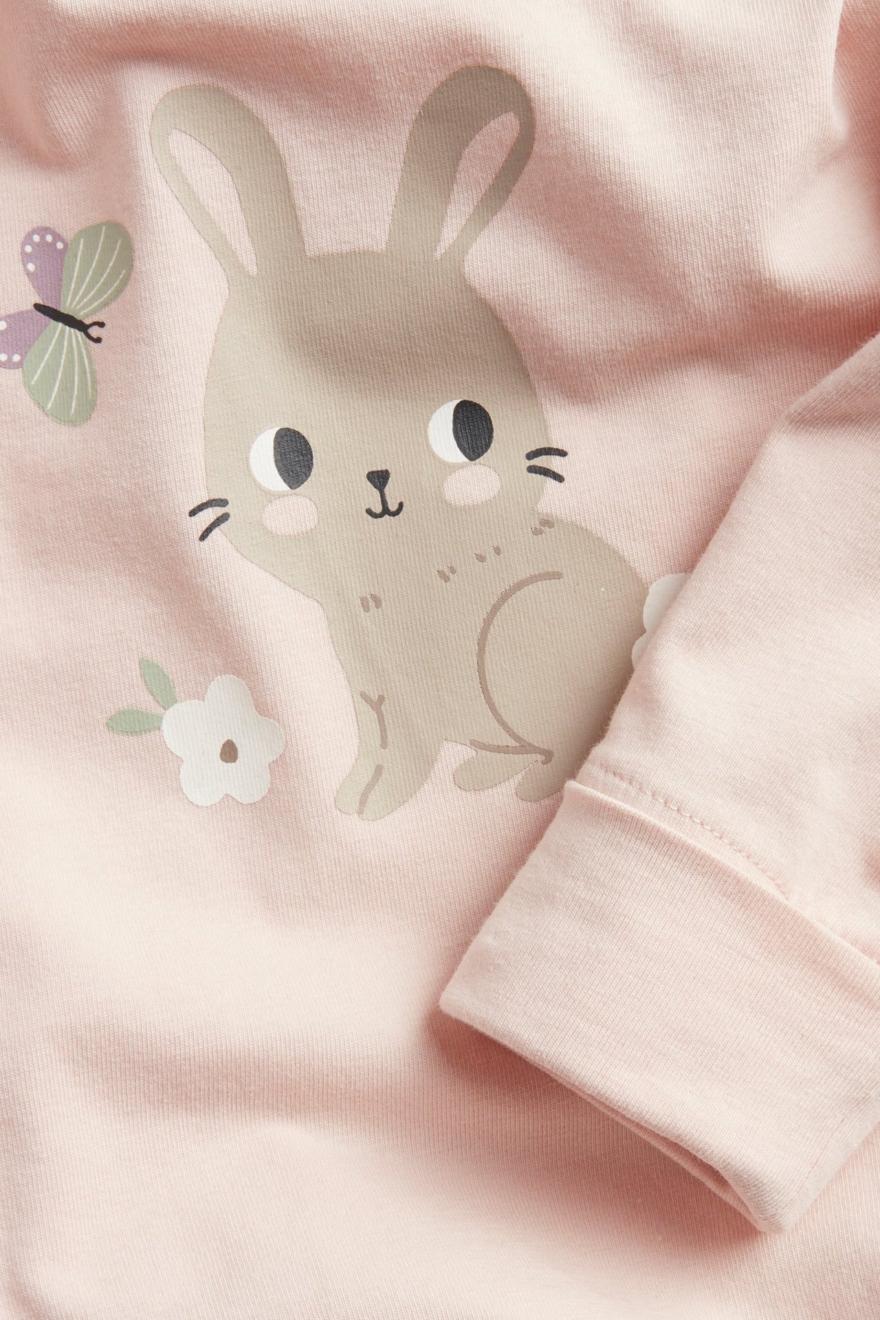 Zbliżenie na różowe bawełniane body niemowlęce z nadrukiem królika i motyla, widać mankiet rękawa.