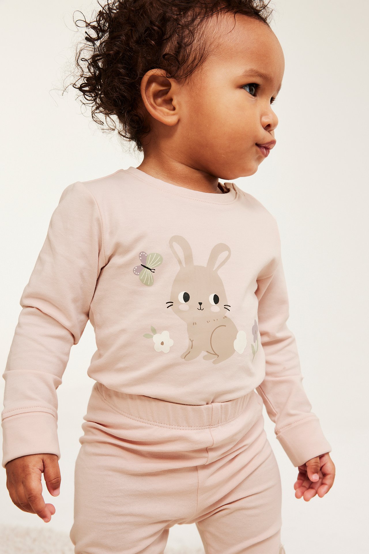 Sivukuva: vauva vaaleanpunaisessa pitkähihaisessa puuvillabodyssa pupukuvioinnilla ja yhteensopivissa housuissa.