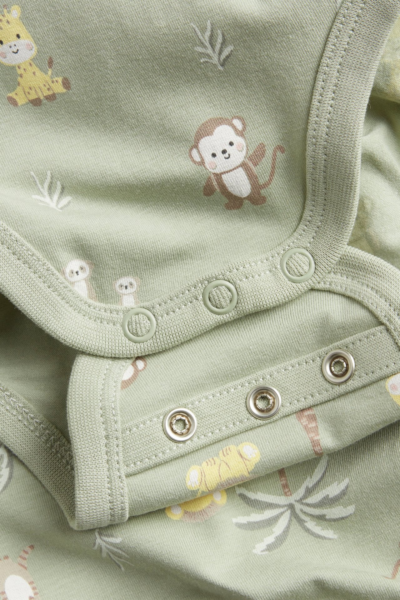 Lähikuva vihreästä kuvioidusta vauvanbodysta, jossa eläinaiheita ja nepparit olkapäässä ja haarassa.