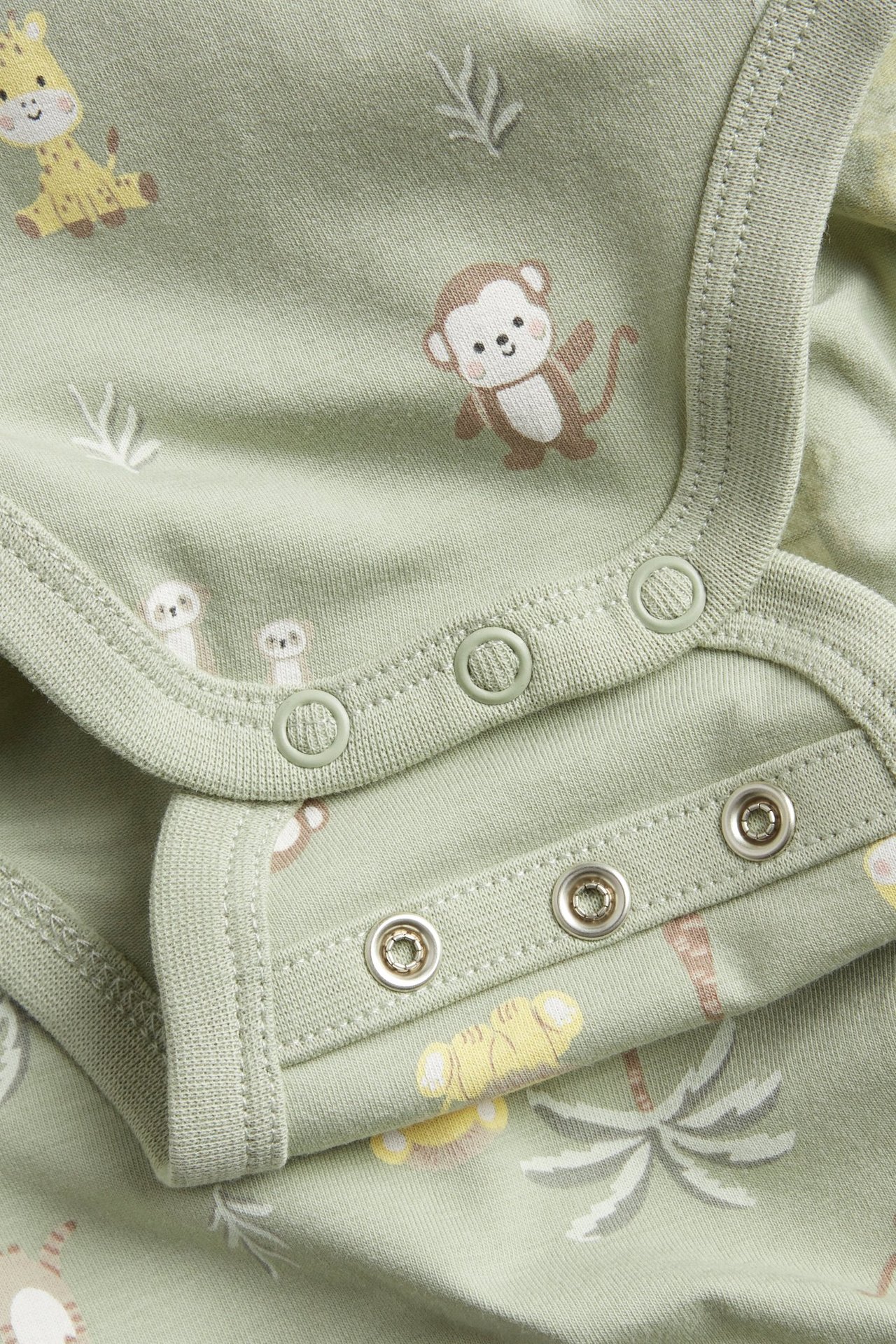 Zbliżenie na zielone body dla niemowląt w zwierzęce wzory, z zatrzaskami na ramieniu i w kroku.