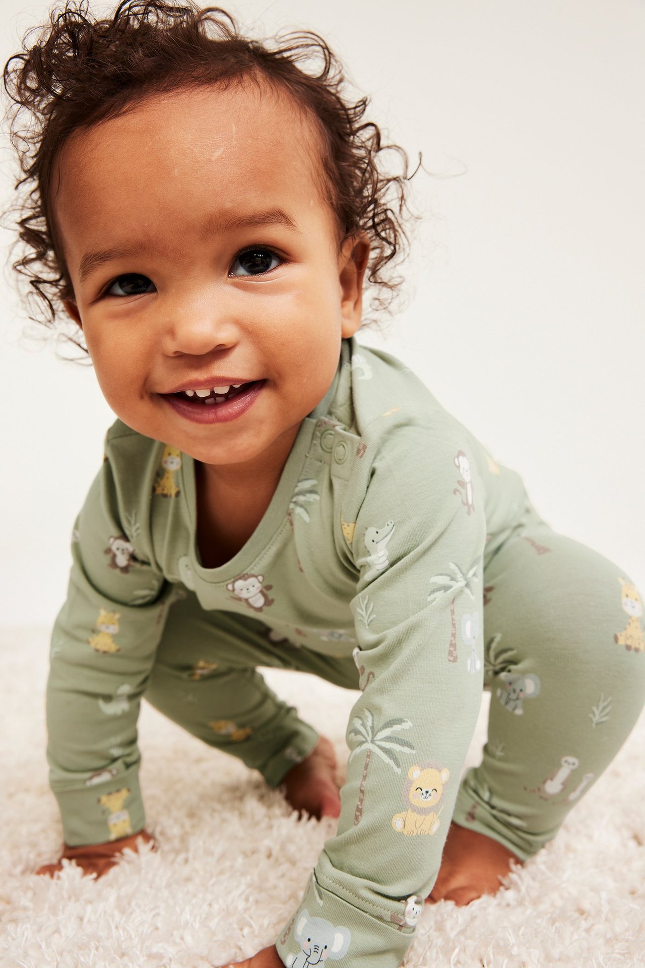 Edestä hymyilevä vauva yllään vihreäkuvioinen puuvillabody, jossa safariteema ja olkapään painonapit.