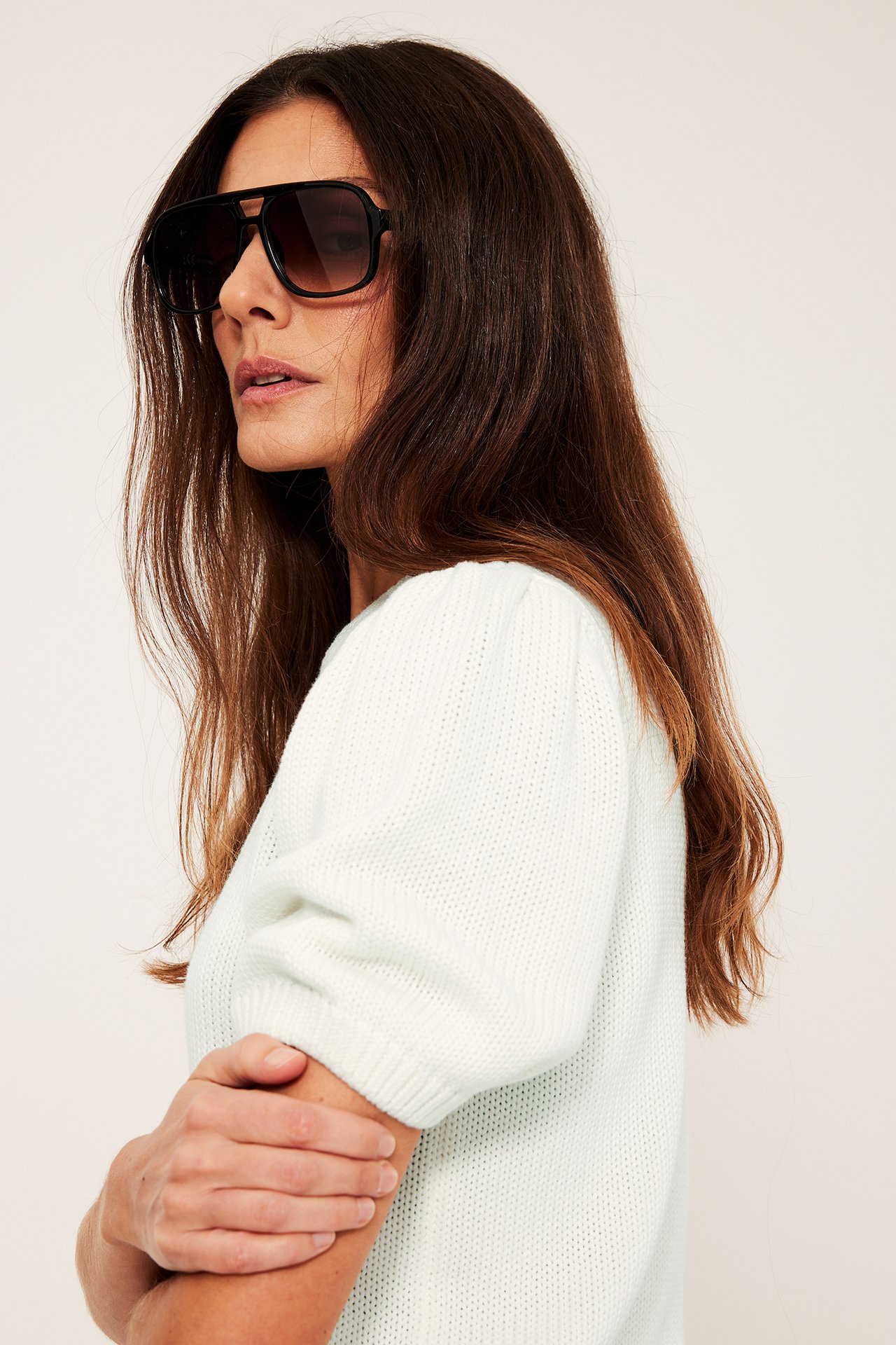 Sidovy av kvinna i offwhite stickad bomullströja med puffärmar och svarta solglasögon.
