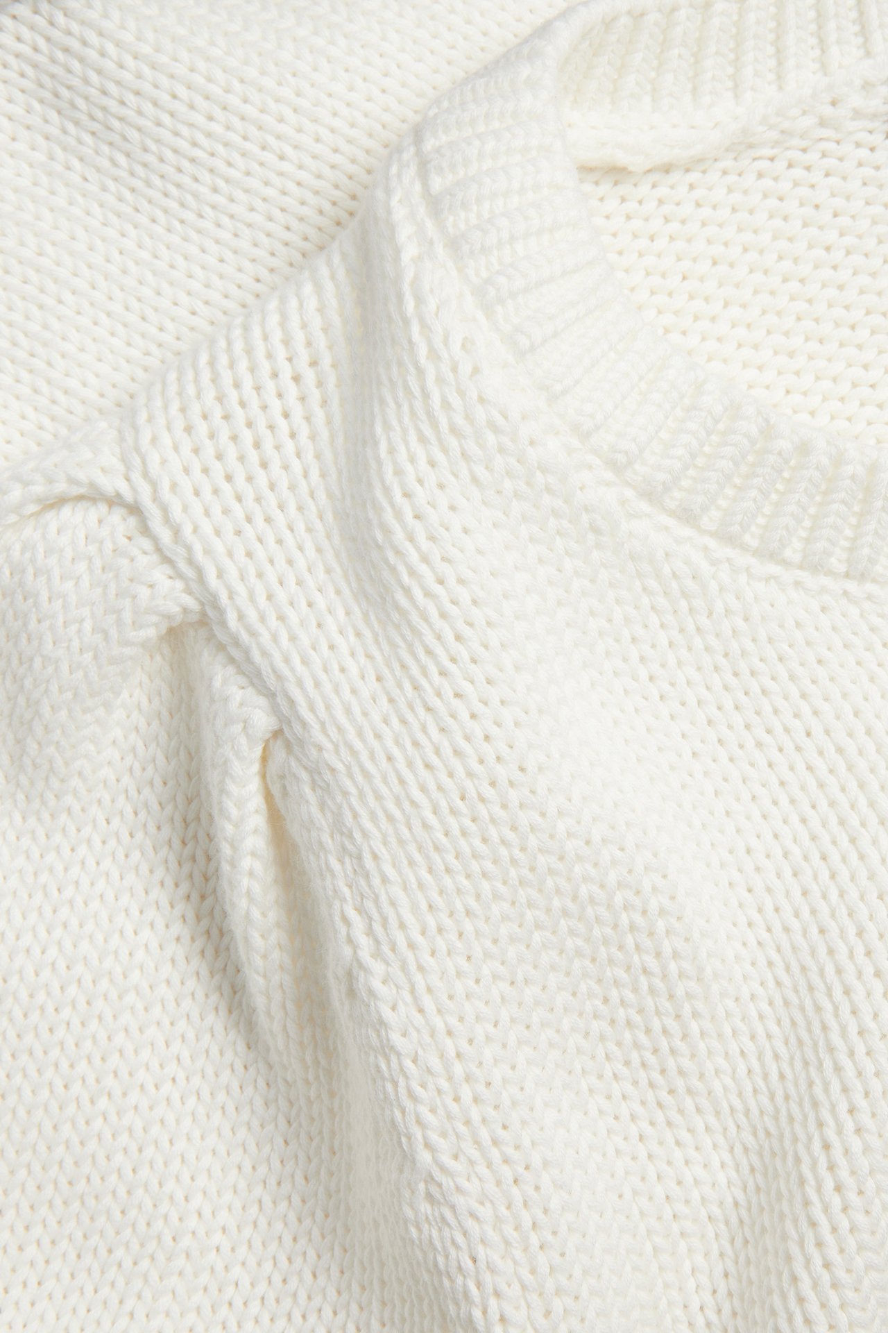 Närbild av en offwhite grovstickad bomullströja med puffärmsdetalj.