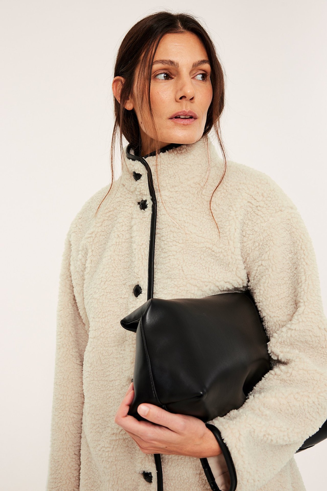 Närbild på en kvinna i offwhite pilejacka med svarta detaljer och knappar, håller en svart handväska.