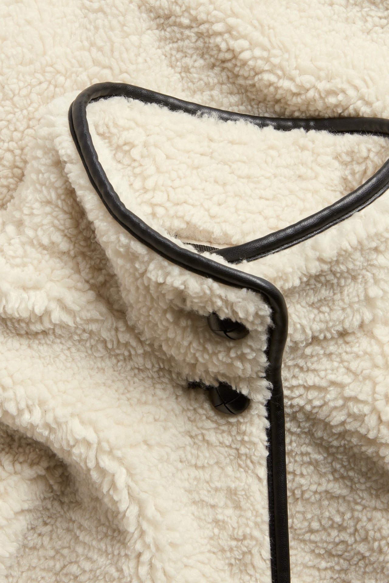 Närbild av en naturvit pilejacka med svarta PU-passpoaler och svarta knappar.