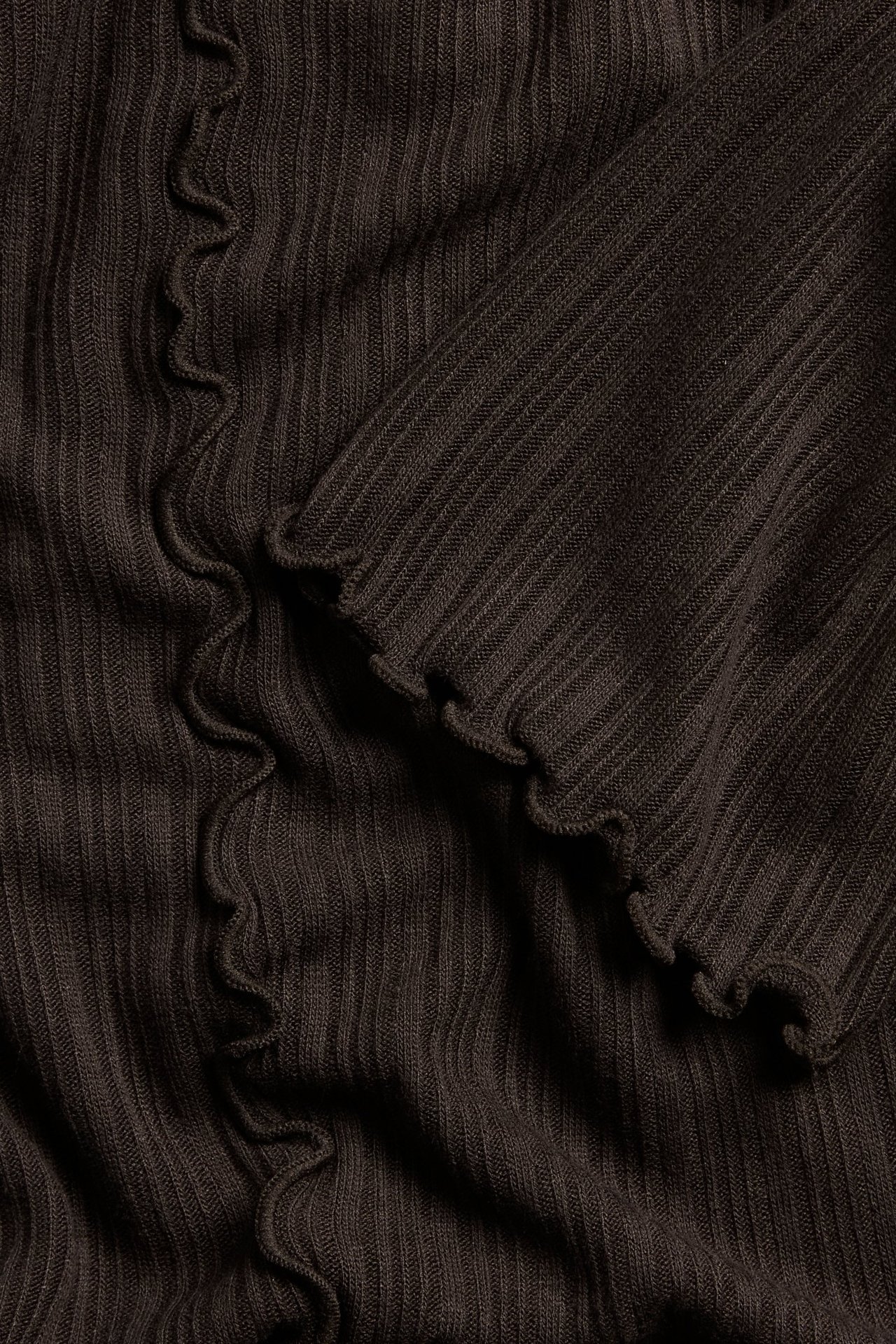 Närbild av en mörkbrun ribbad viskos-elastan topp med vågiga babyoverlockkanter.