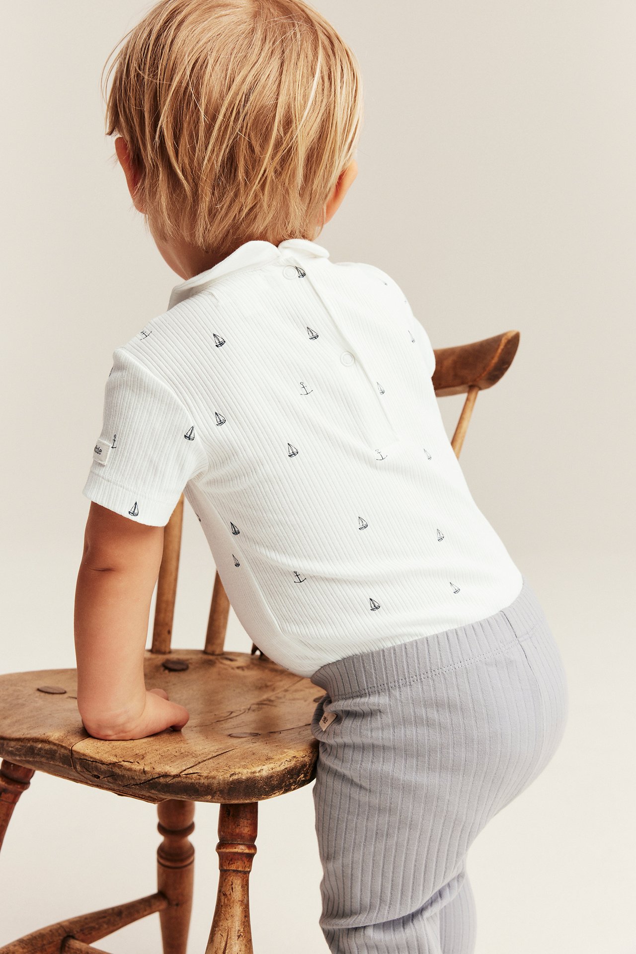 Bakside av baby i offwhite ribbet kortermet body med seilbåter og grå ribbete leggings.