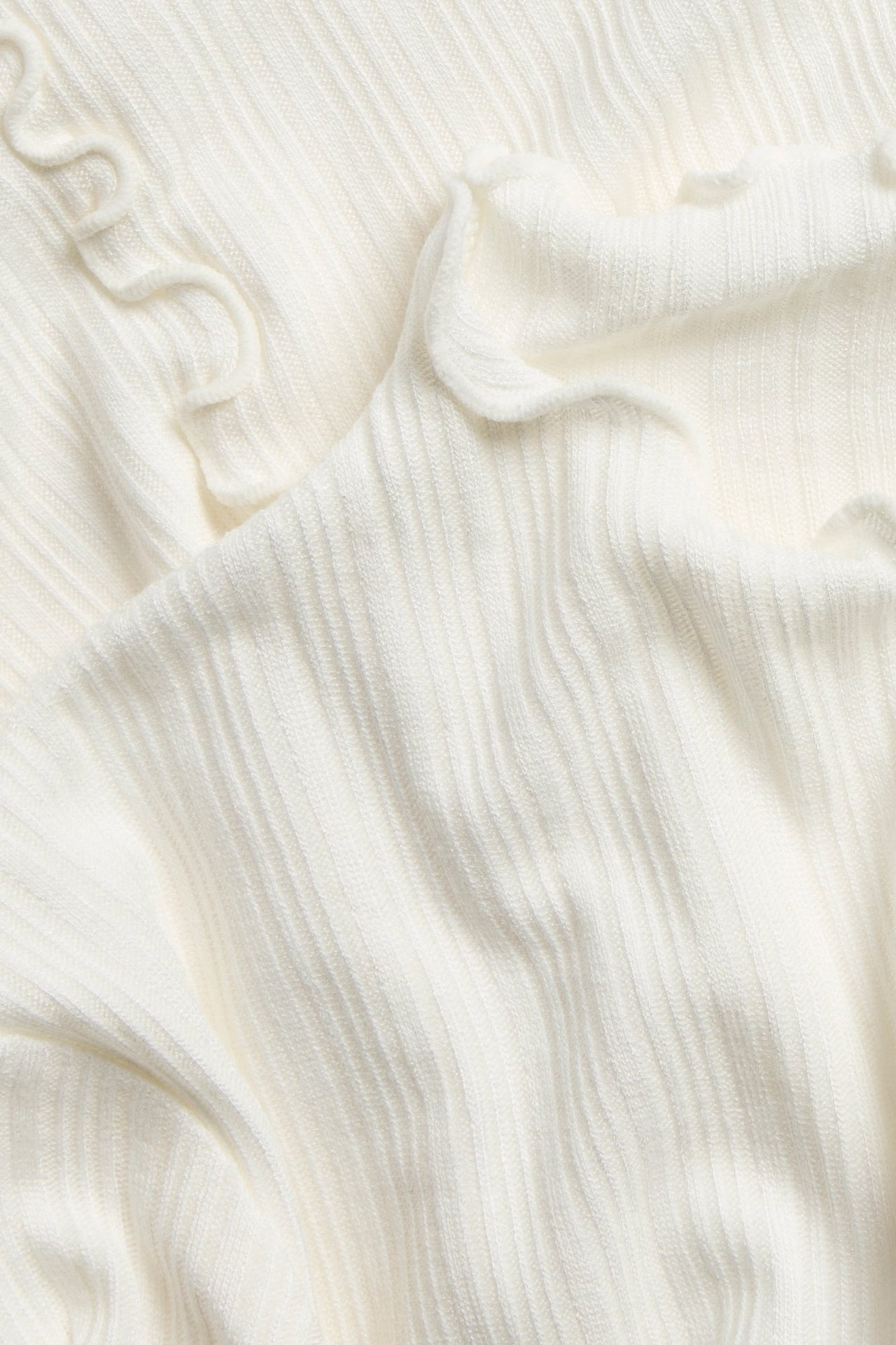 Närbild av en offwhite ribbad långärmad topp med fina babyoverlockkanter.