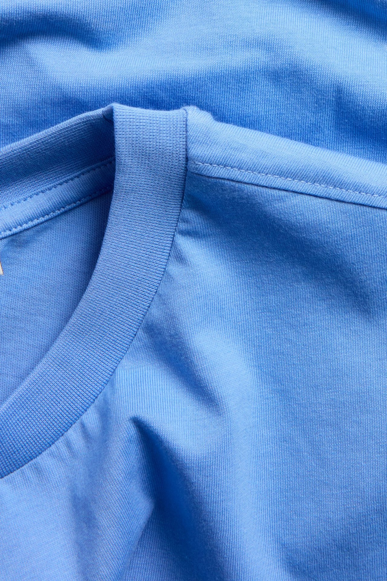 Lähikuva sinisestä ylisuuresta laatikkomaisesta puuvilla-T-paidasta, jossa näkyy resori pääntie ja sileä kangas.