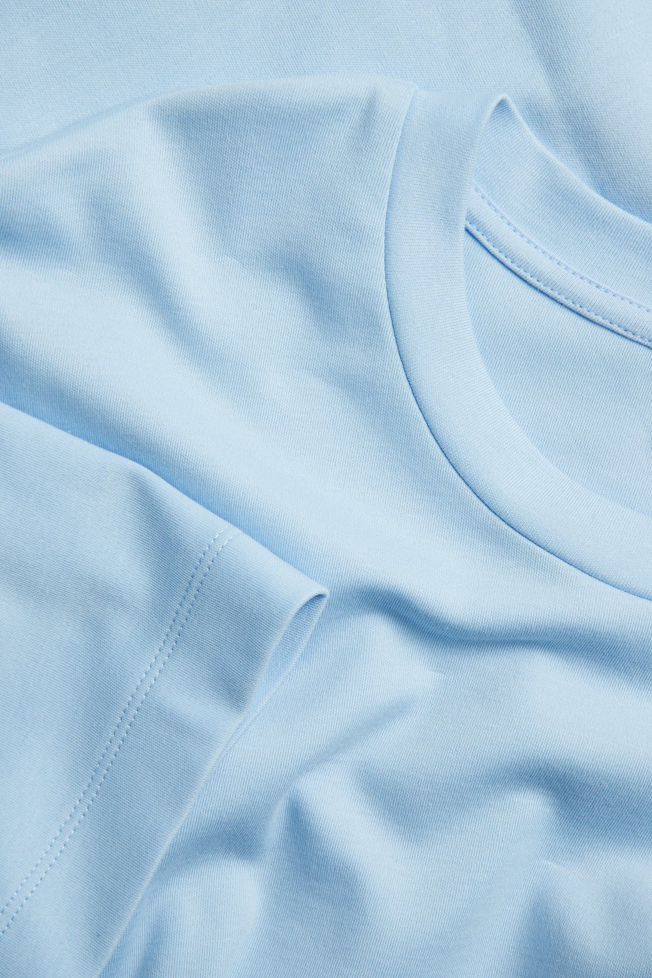 Zbliżenie: jasnoniebieski, oversize'owy t-shirt z bawełny interlock, z prążkowanym dekoltem i krótkimi rękawami.