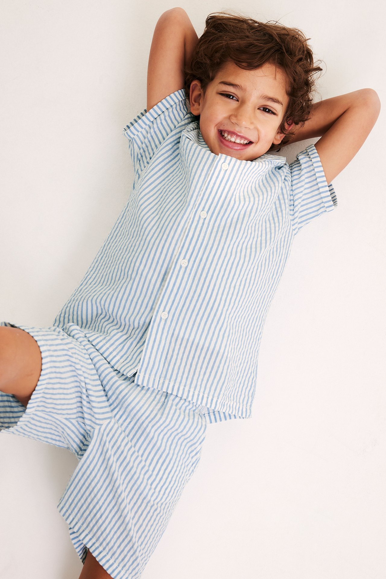 Ovanifrånvy av ett leende barn i en blåvit randig kortärmad skjorta och matchande shorts i bäckebölja.