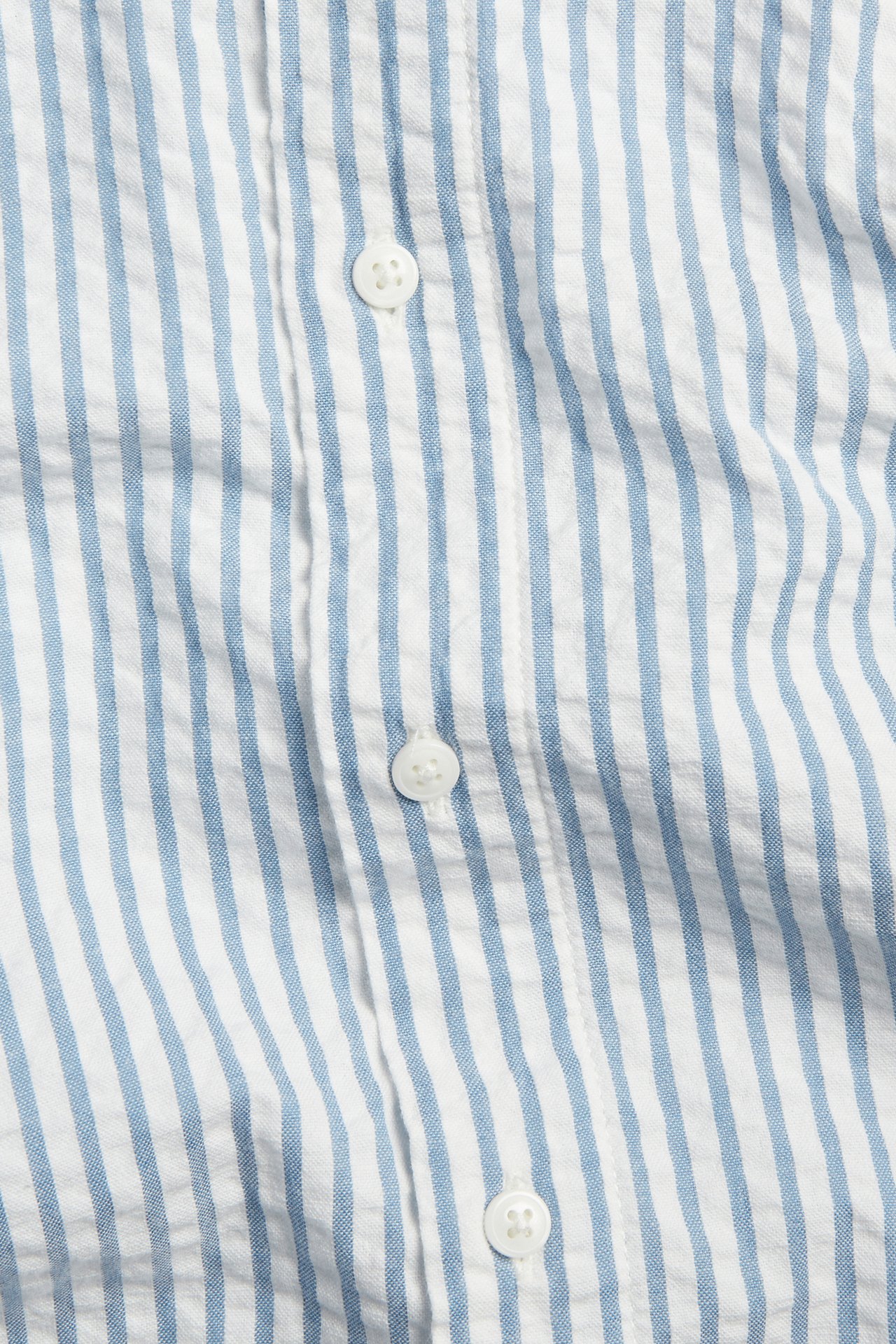 Zbliżenie na niebiesko-białą koszulę w paski z bawełny seersucker z białymi guzikami.