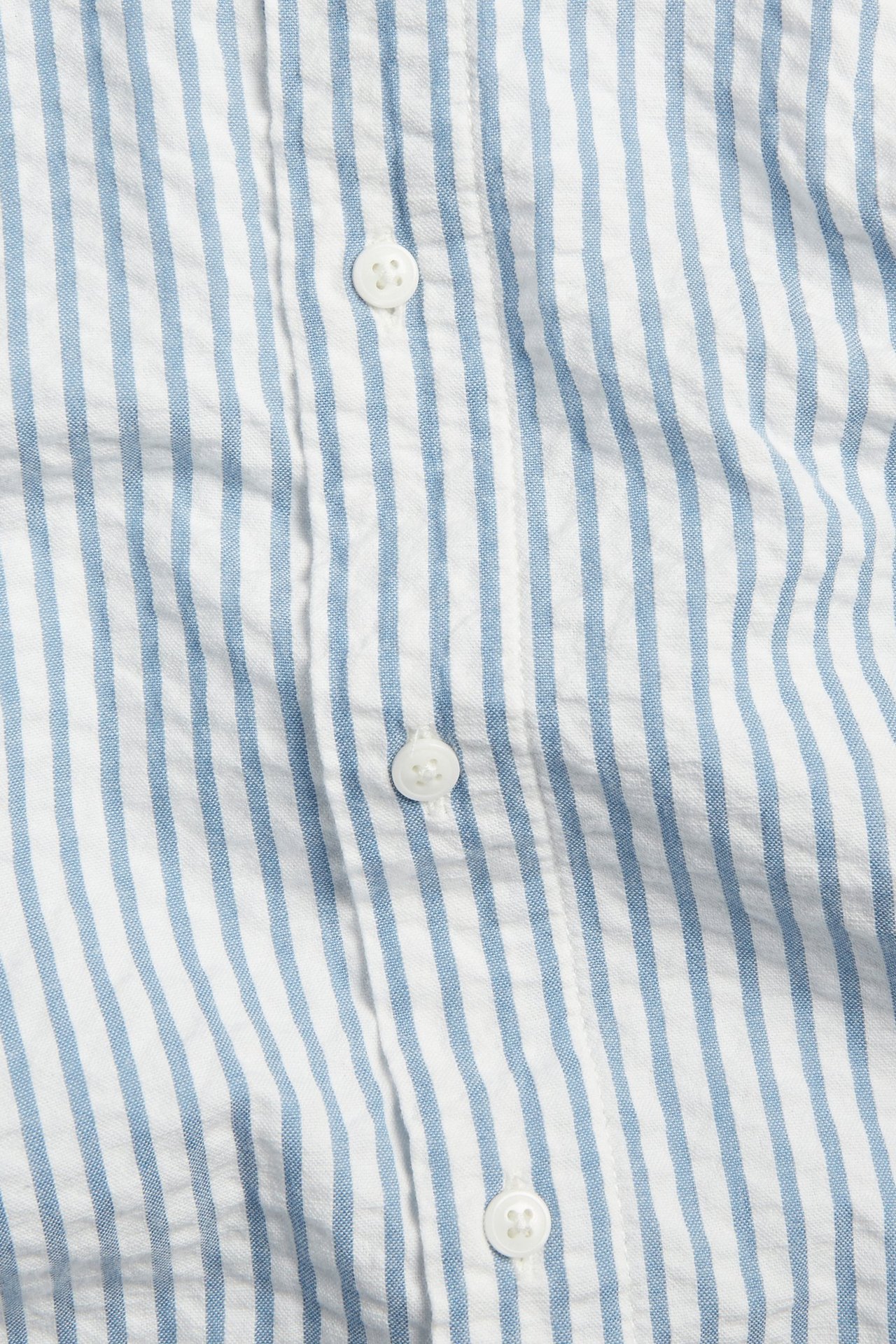Zbliżenie na niebiesko-białą koszulę w paski z bawełny seersucker z białymi guzikami.