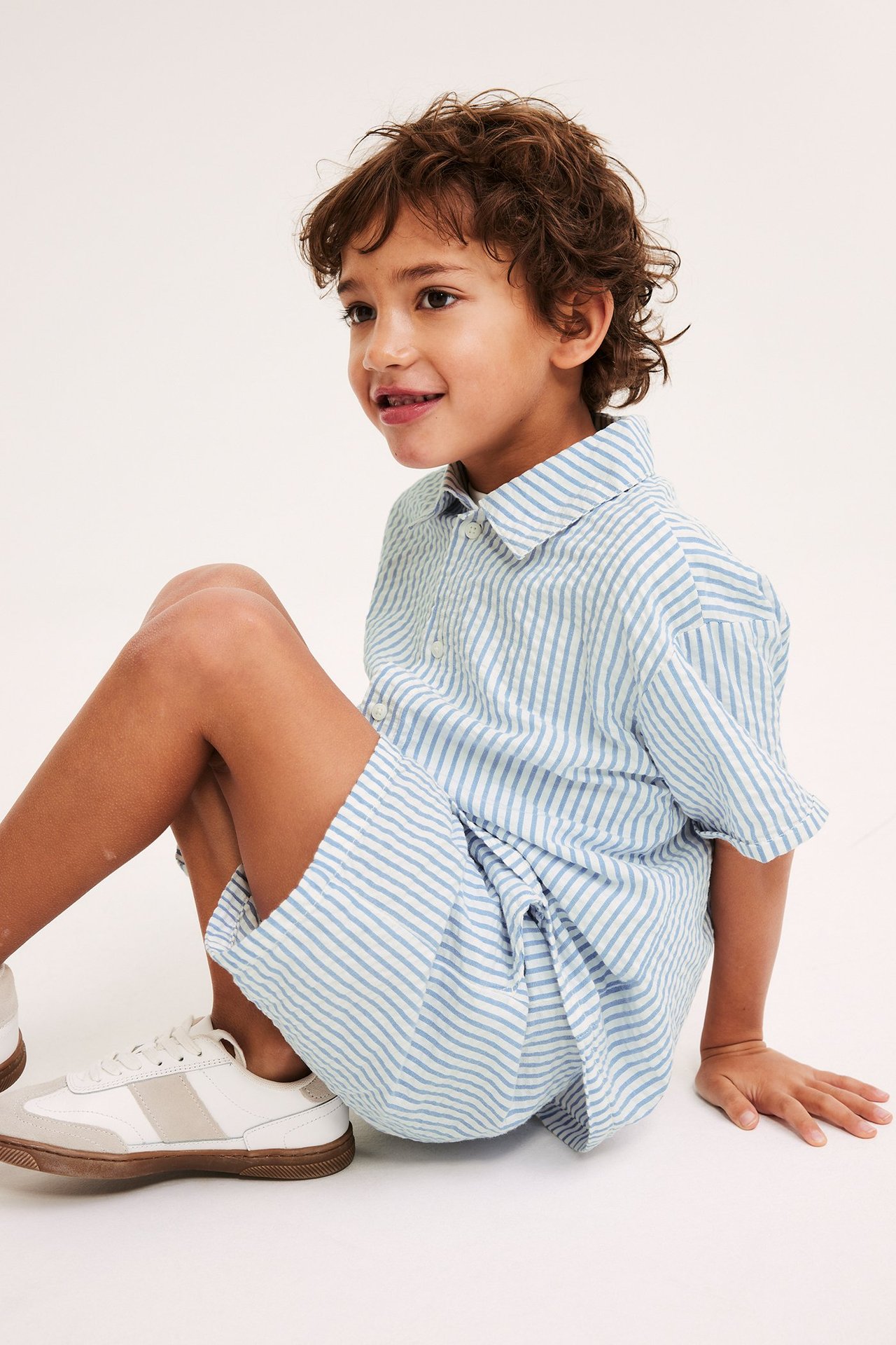 Edestä: Poika siniraidallisissa puuvillashortseissa, yhteensopiva paita, valkoiset tennarit.